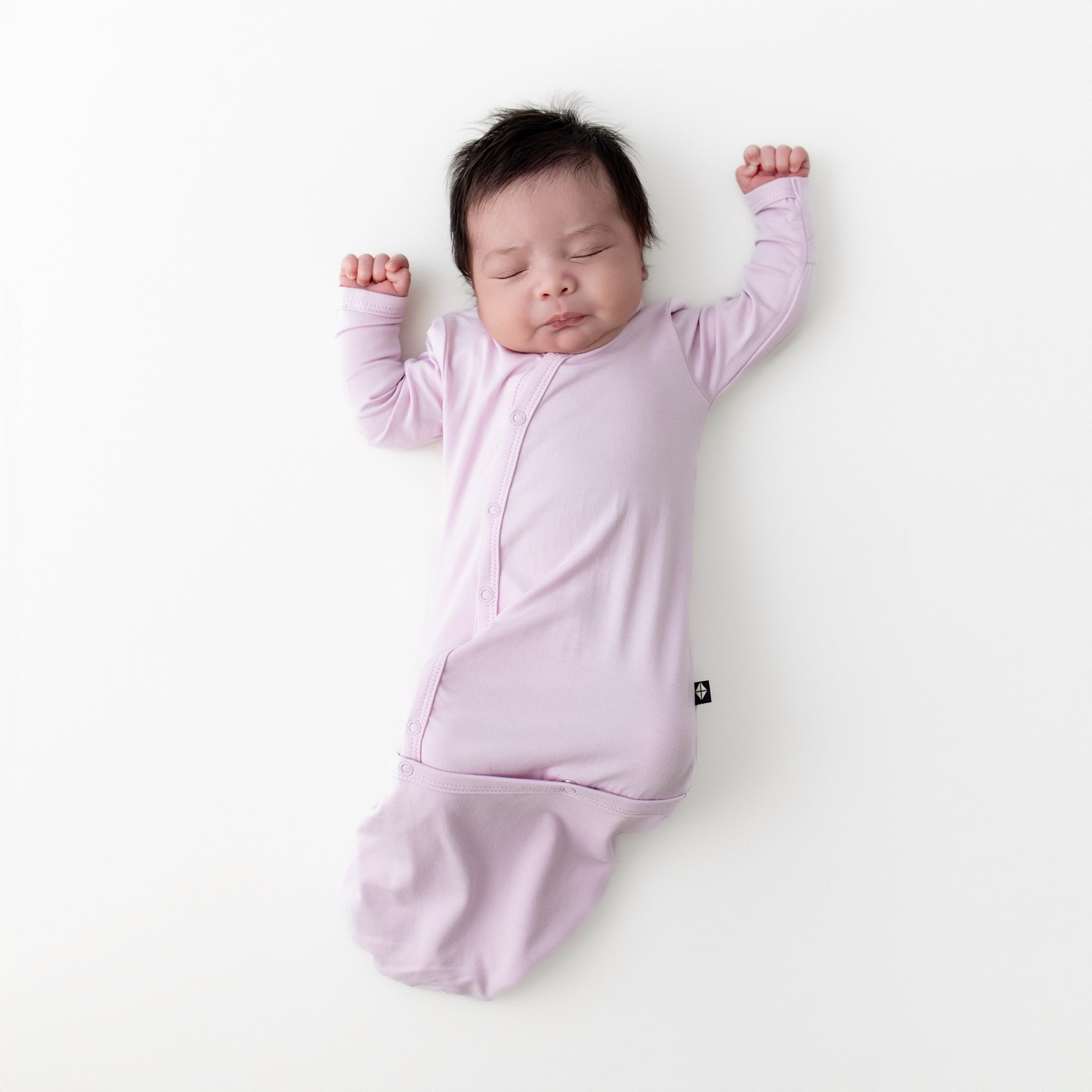 Sleeping infant wearing the Bundler in Thistle laying on a white surface