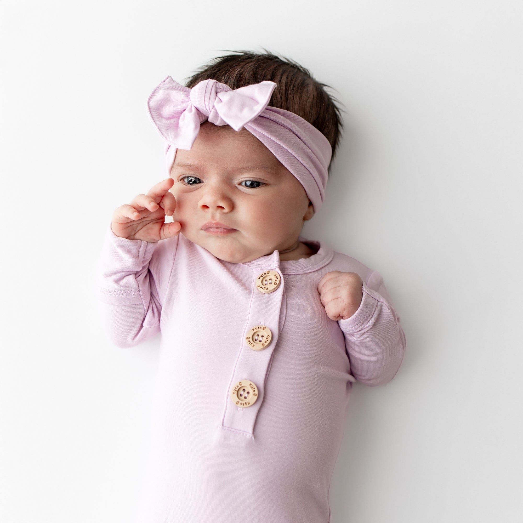 Baby wearing a light purple outfit with buttons and a matching headband on a white background