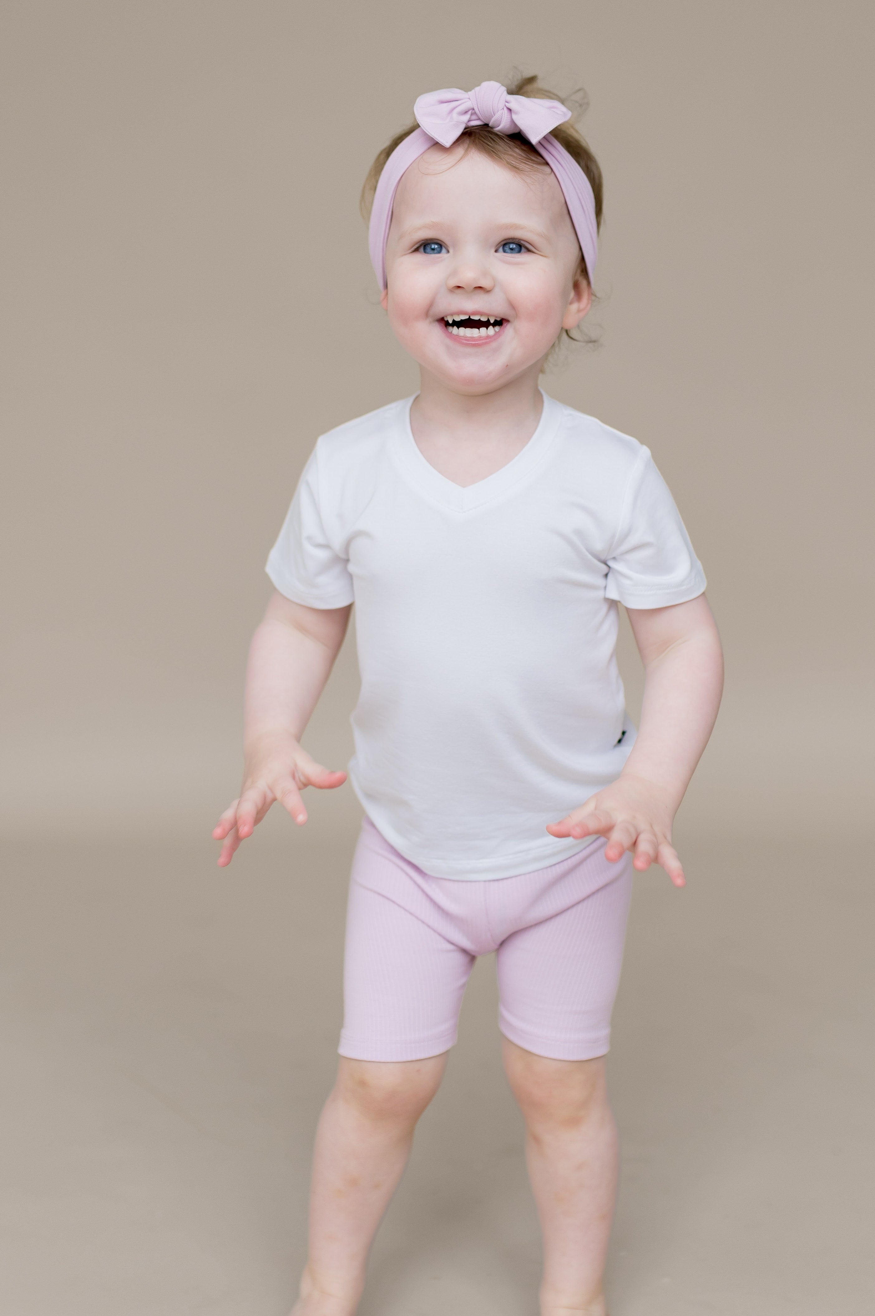 Young smiling toddler girl wearing the Ribbed Toddler Biker Shorts in Thistle paired with a white v-neck