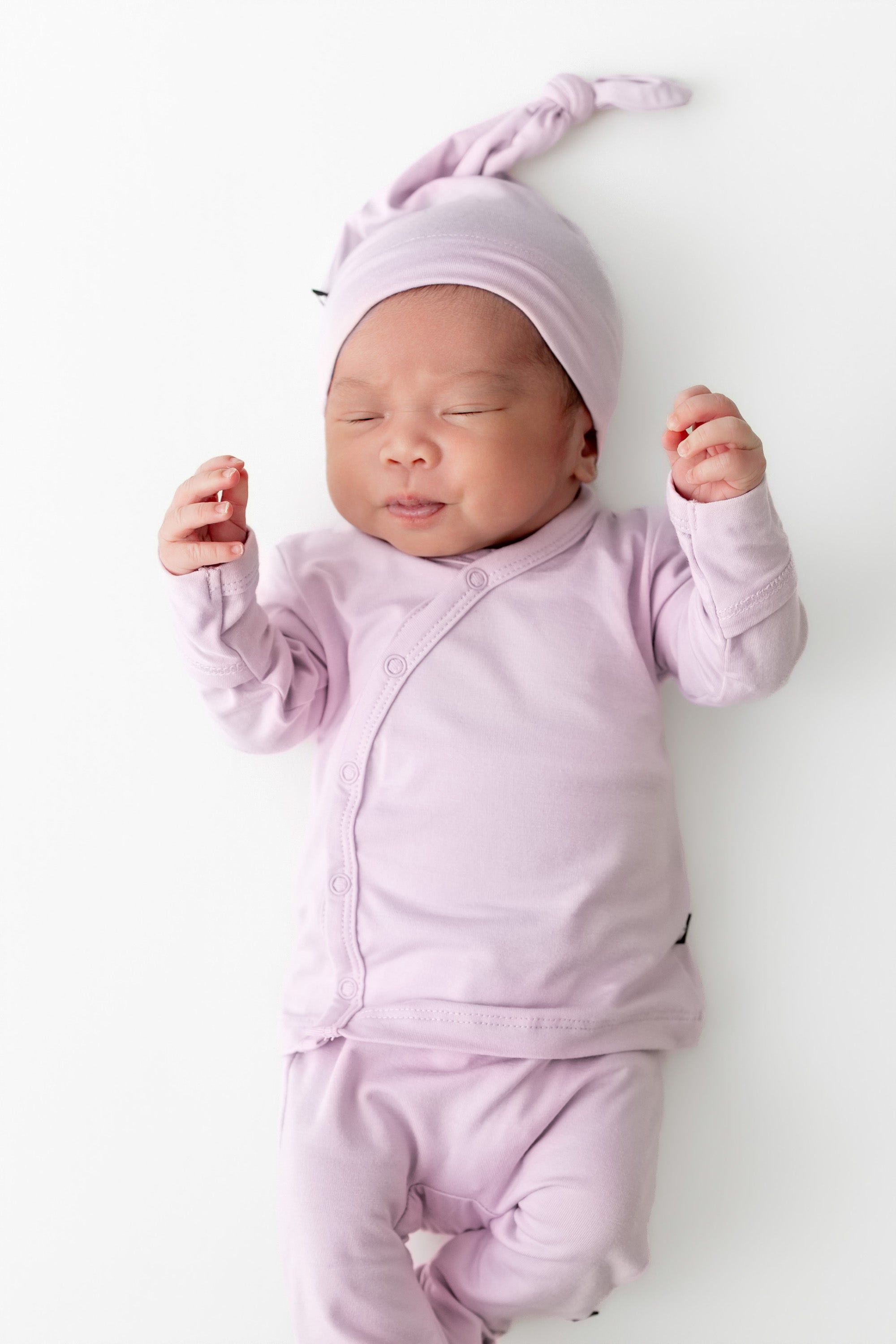 Newborn baby in a light purple outfit and hat lying on a white background
