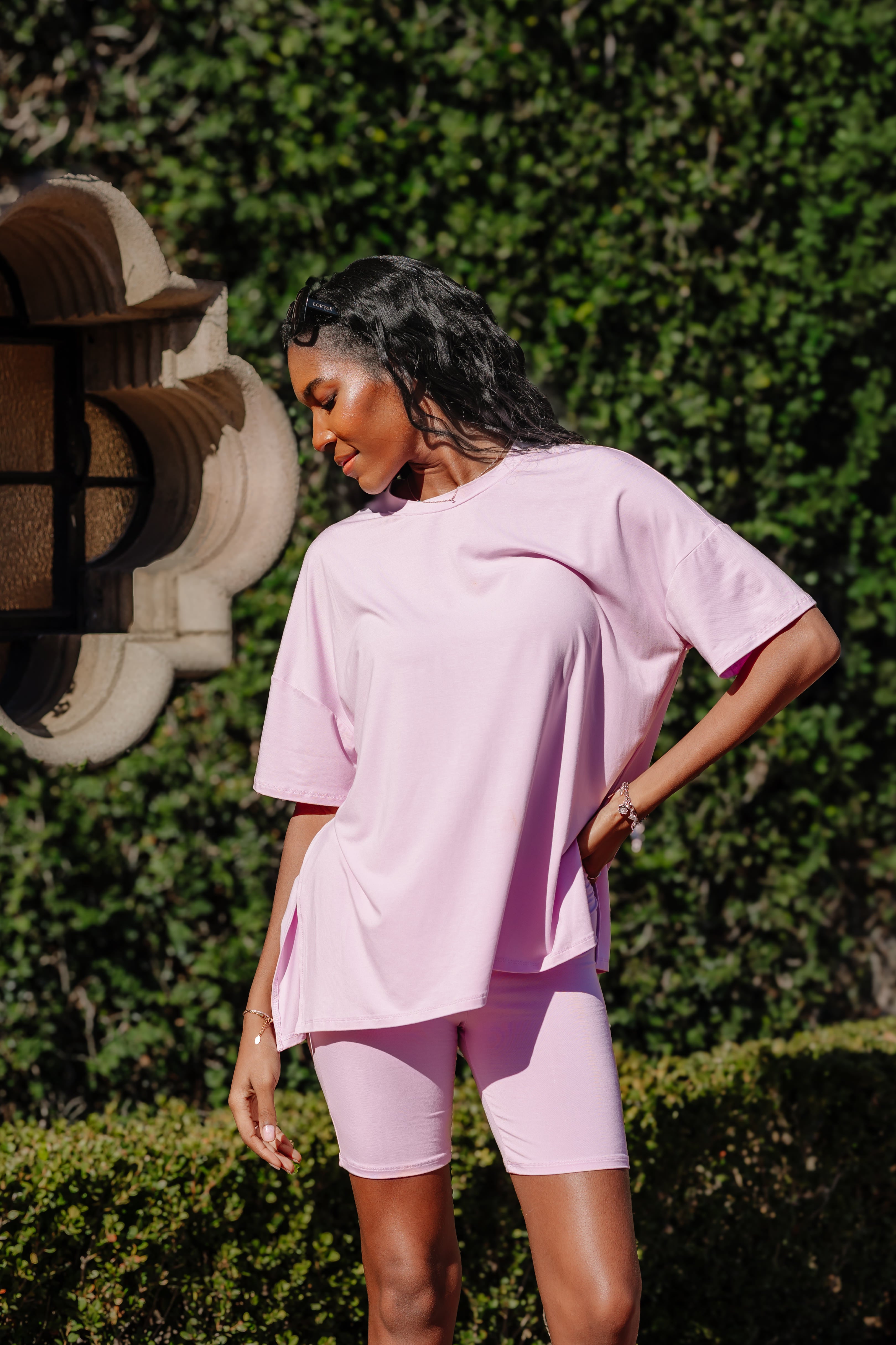 Woman wearing a light purple biker short outfit standing outdoors with greenery in the background