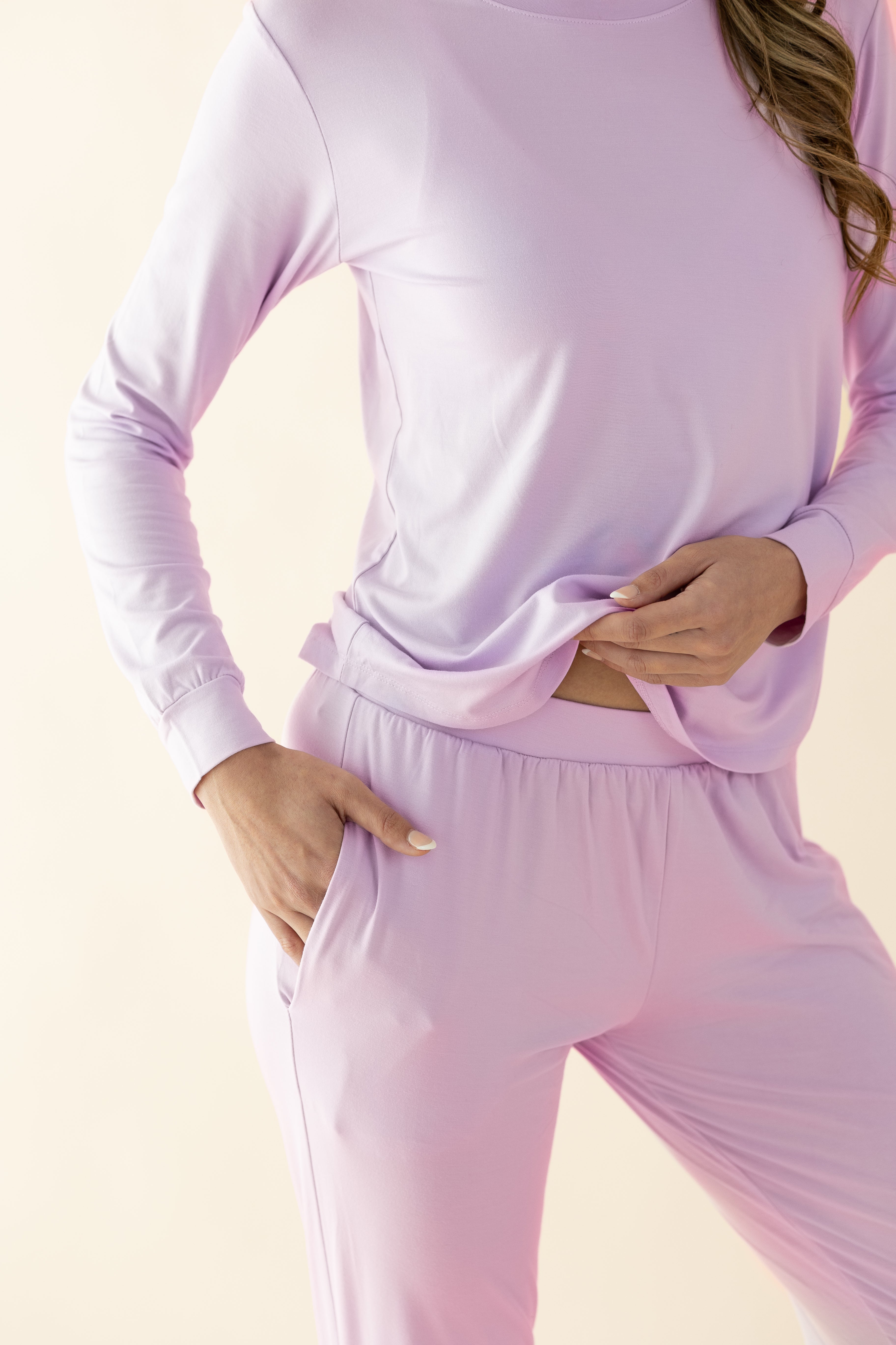 Person wearing a light purple long-sleeve top and jogger style pants on a beige background