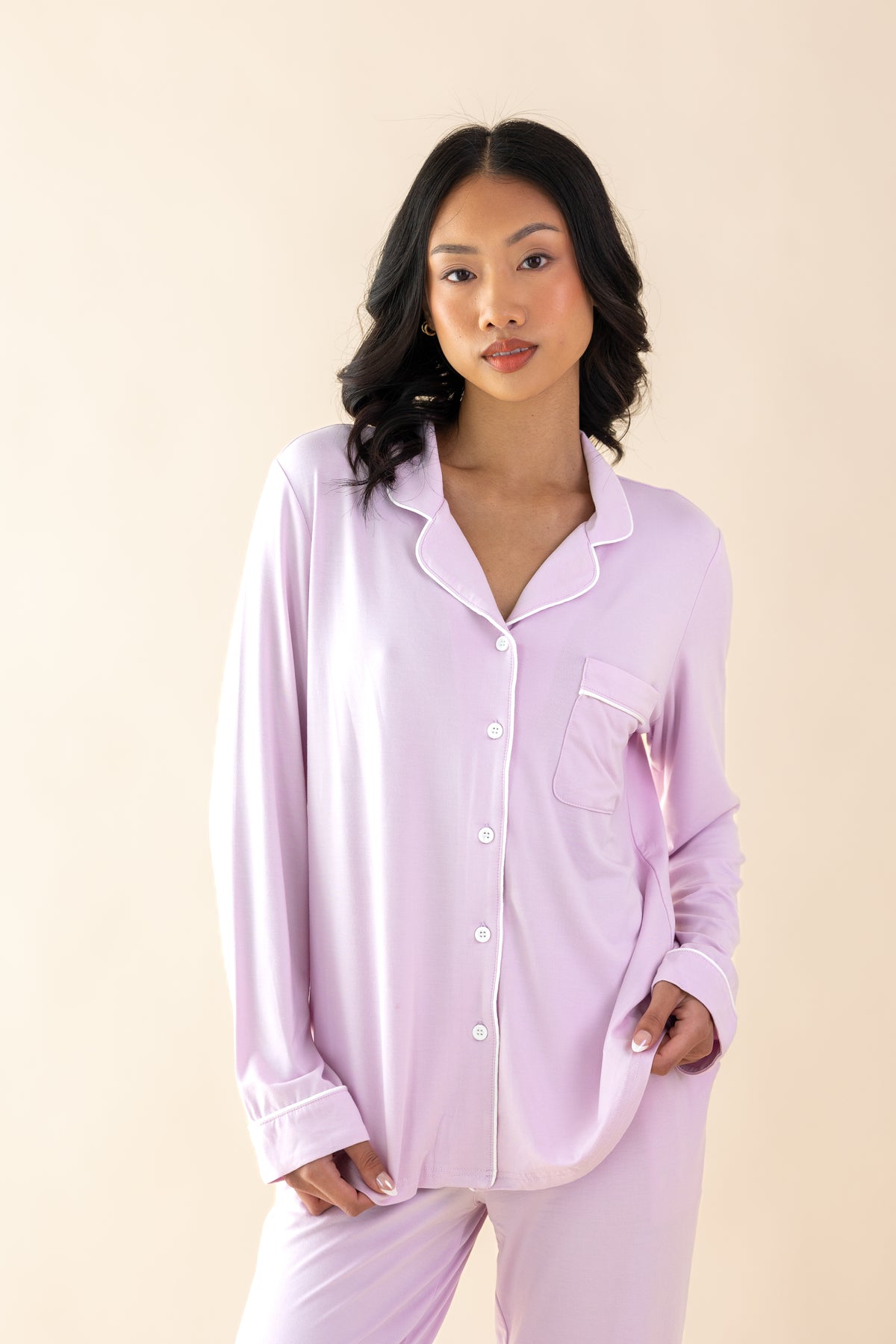Woman wearing a light purple pajama set with white piping against a beige background