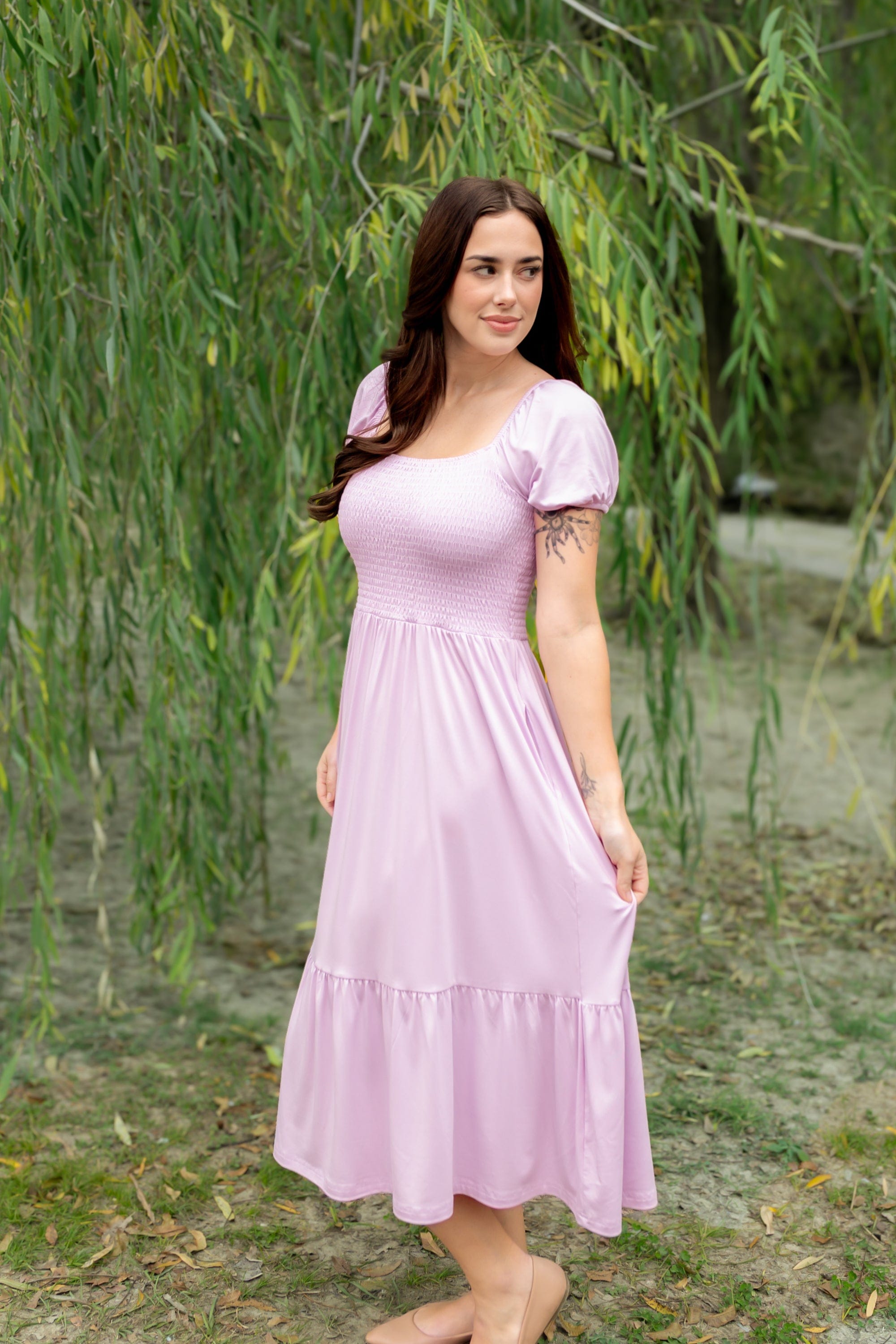 Woman in a purple dress standing outdoors with greenery in the background