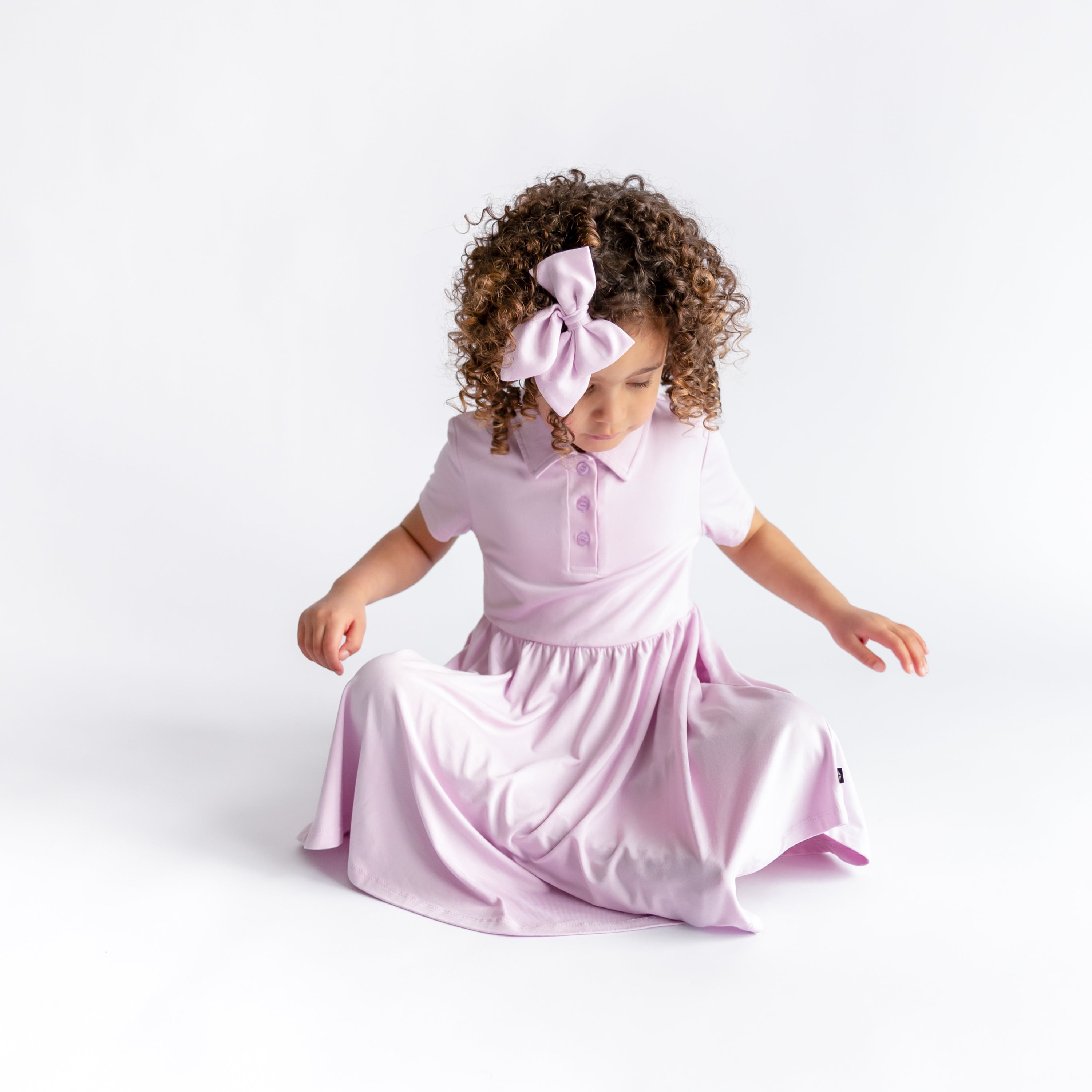 Young girl sitting on the floor wearing the Polo Dress in Thistle