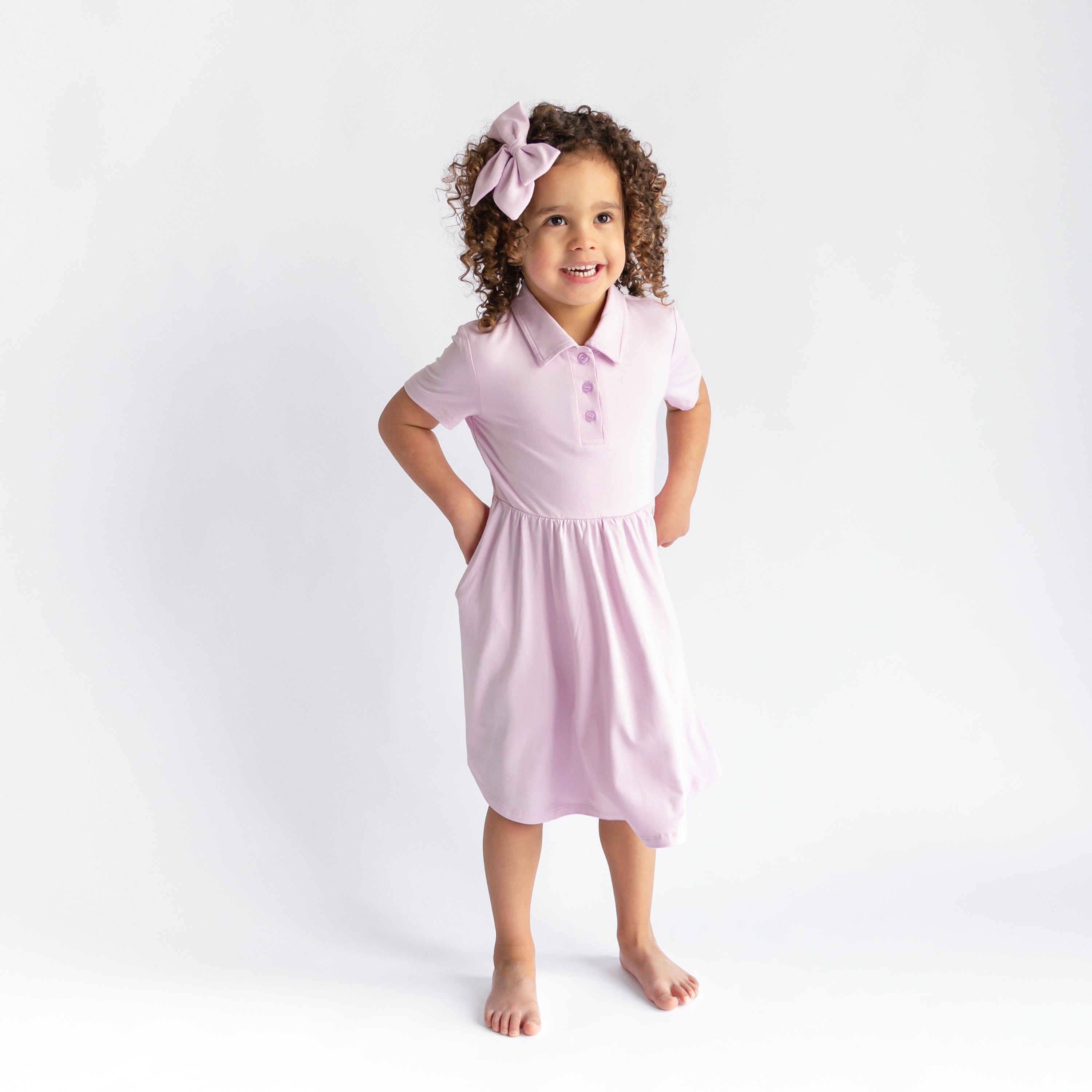 Young girl modeling the Polo Dress in Thistle standing in front of a white background