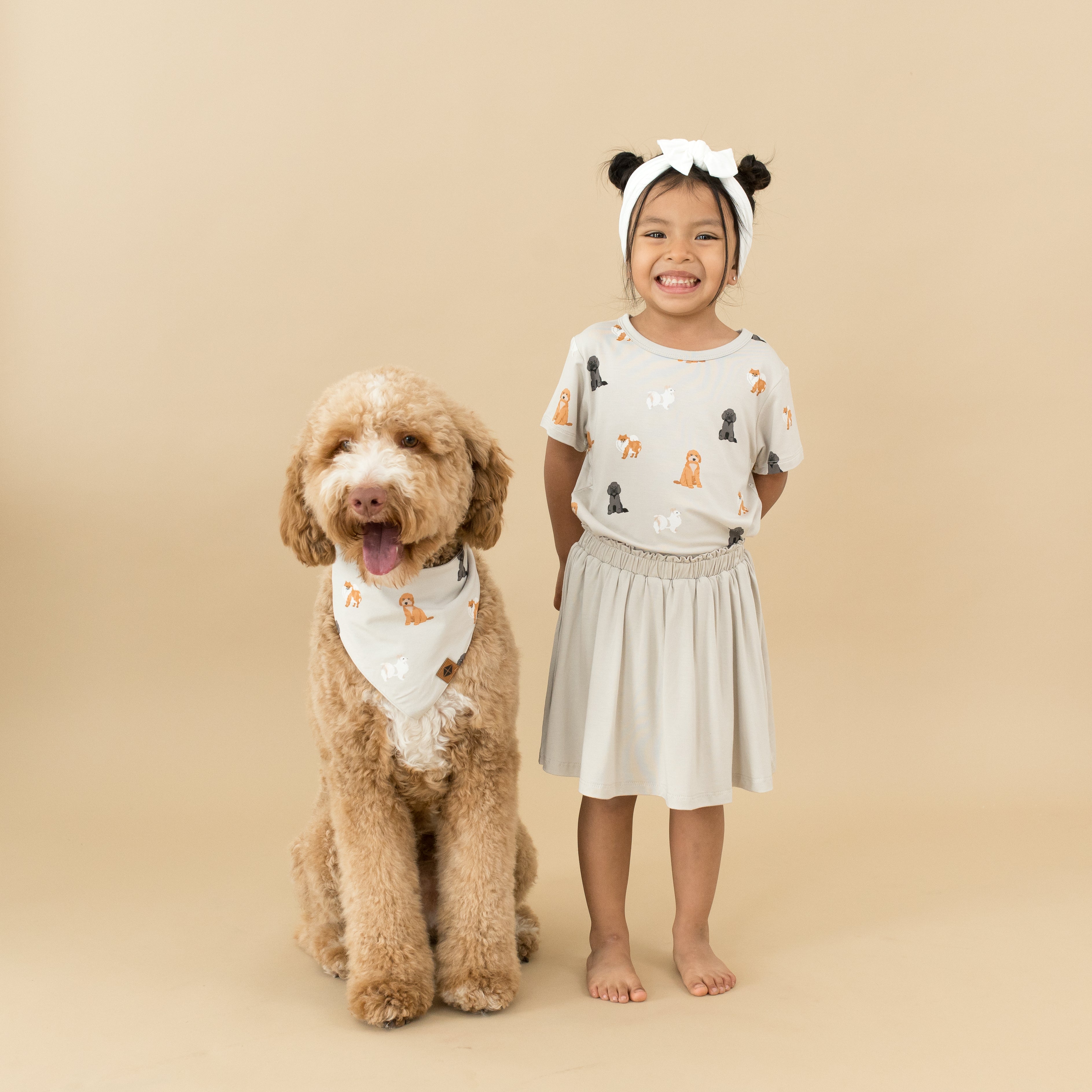 Child wearing Toddler Basic Tee in Fluffy Dog and Oat Skort next to dog wearing matching bandana