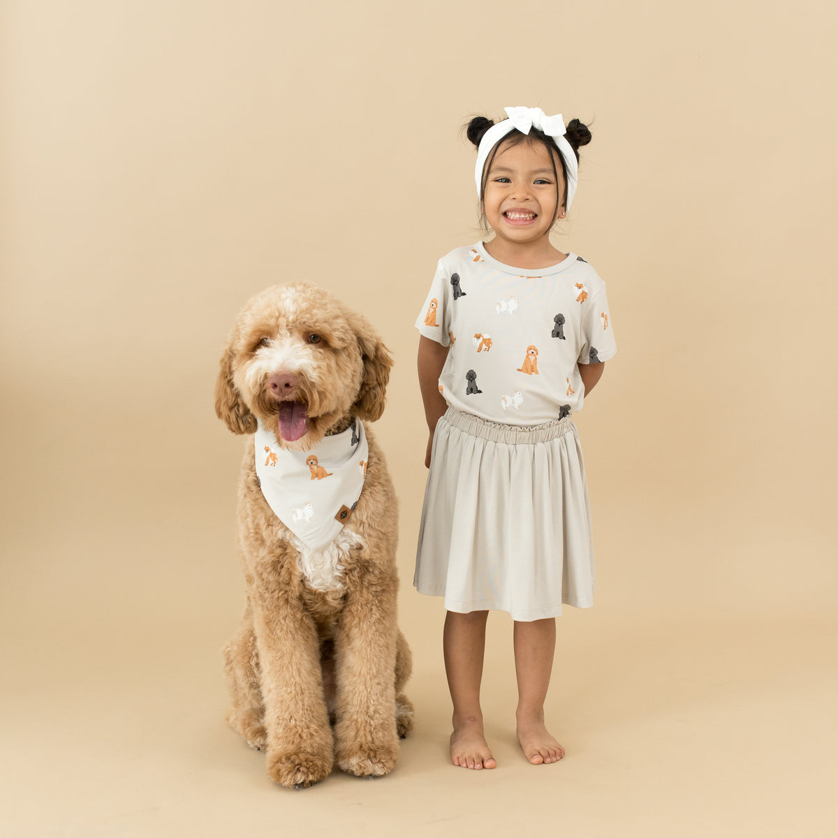 Child wearing Toddler Basic Tee in Fluffy Dog and Oat Skort next to dog wearing matching bandana