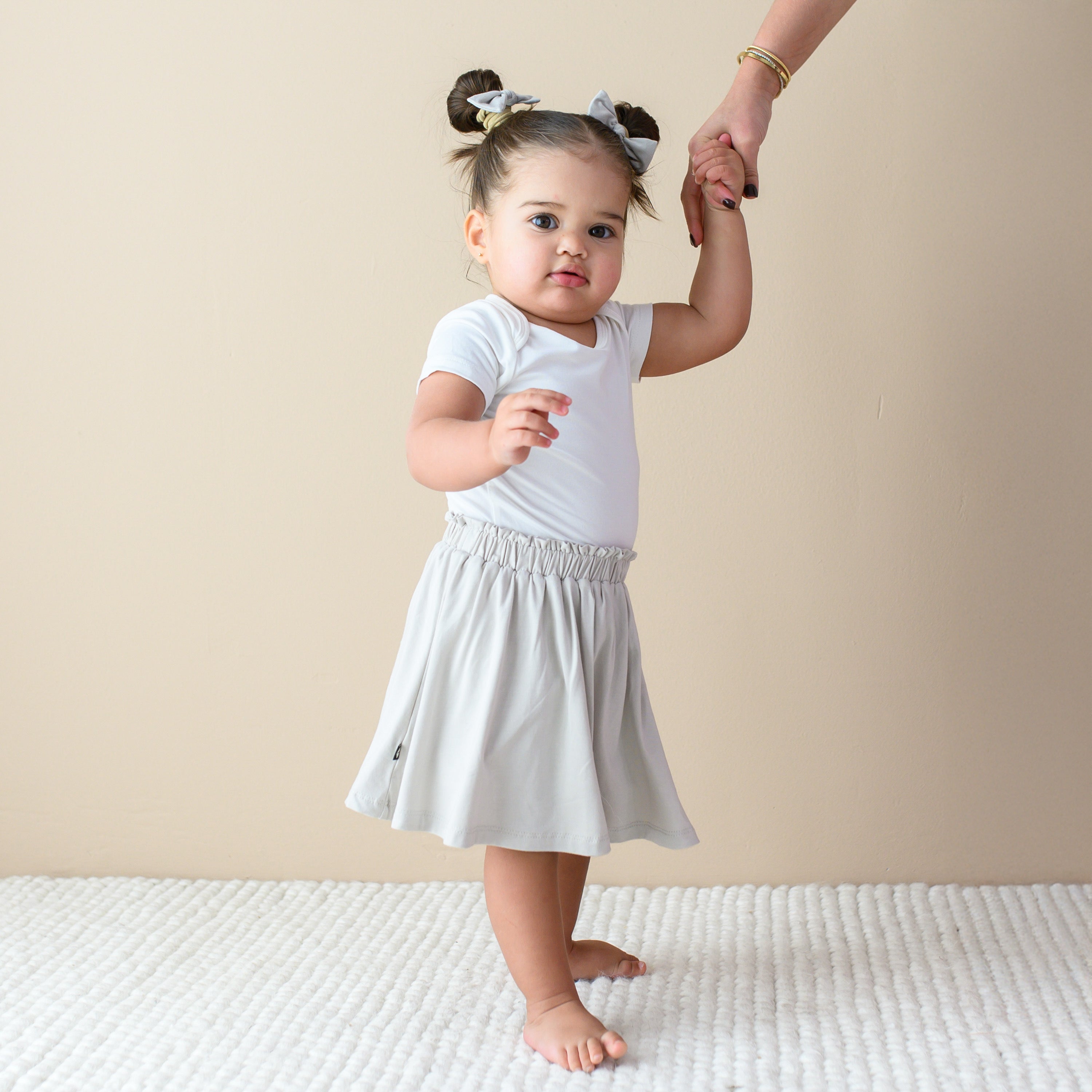 Toddler holding an adult's hand while wearing Skort in Oat and Short Sleeve Bodysuit in Cloud