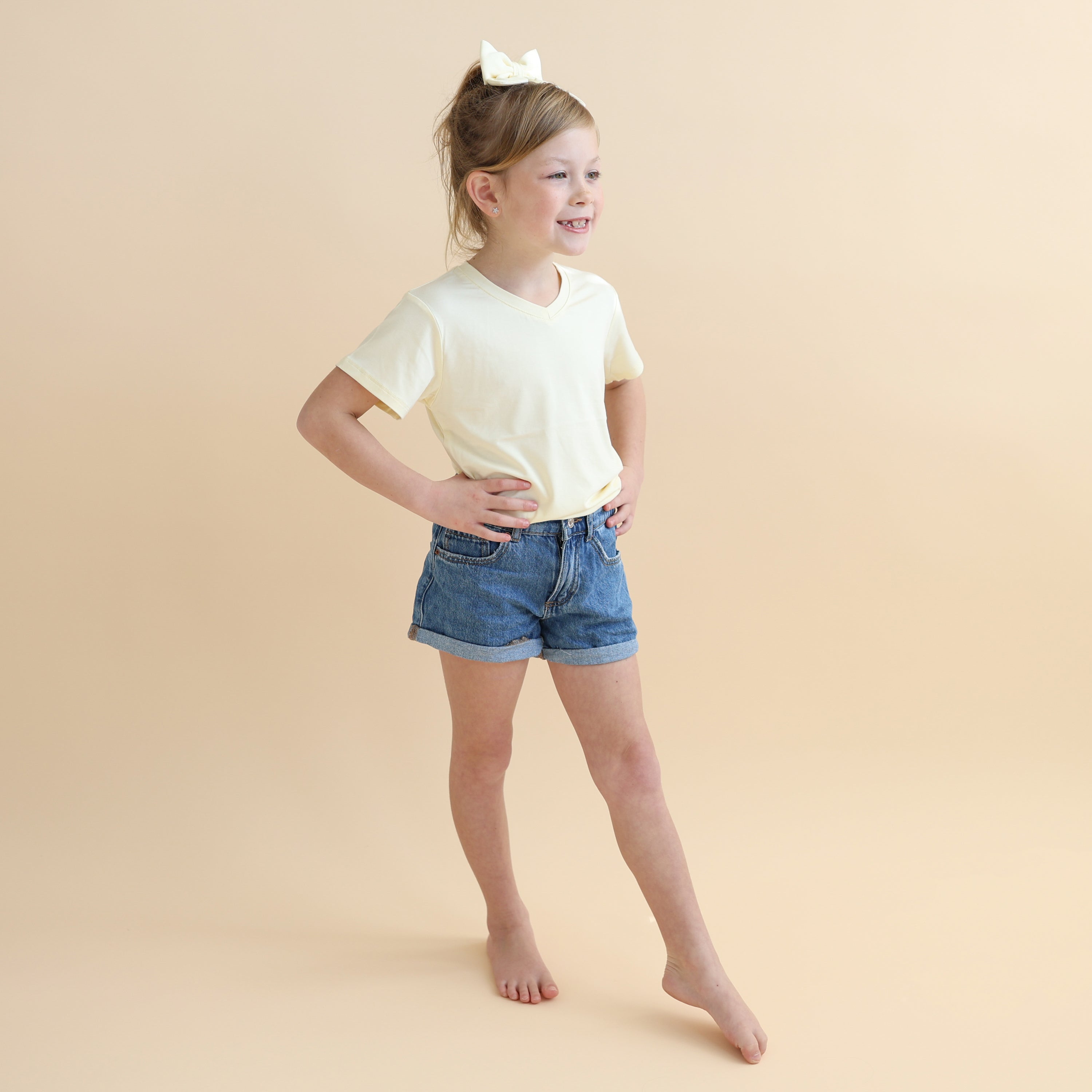 Young girl posing wearing the Toddler V-Neck Tee in Chamomile with jean shorts