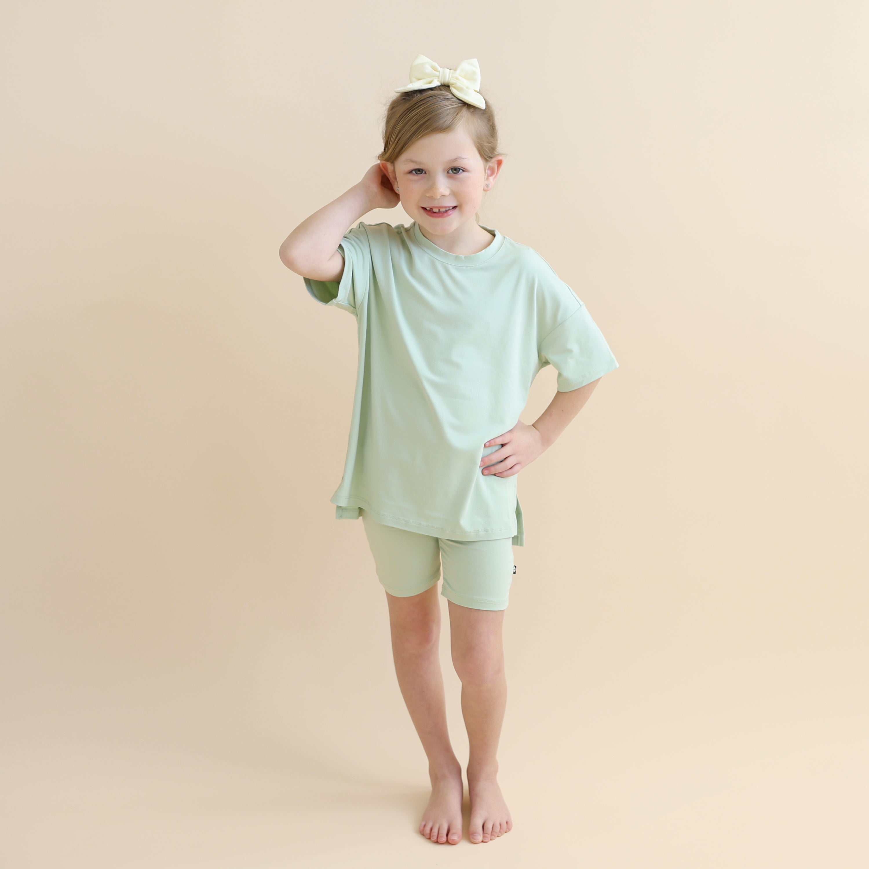 Young girl standing in front of a light neutral background wearing the Toddler Biker Short Set in Basil