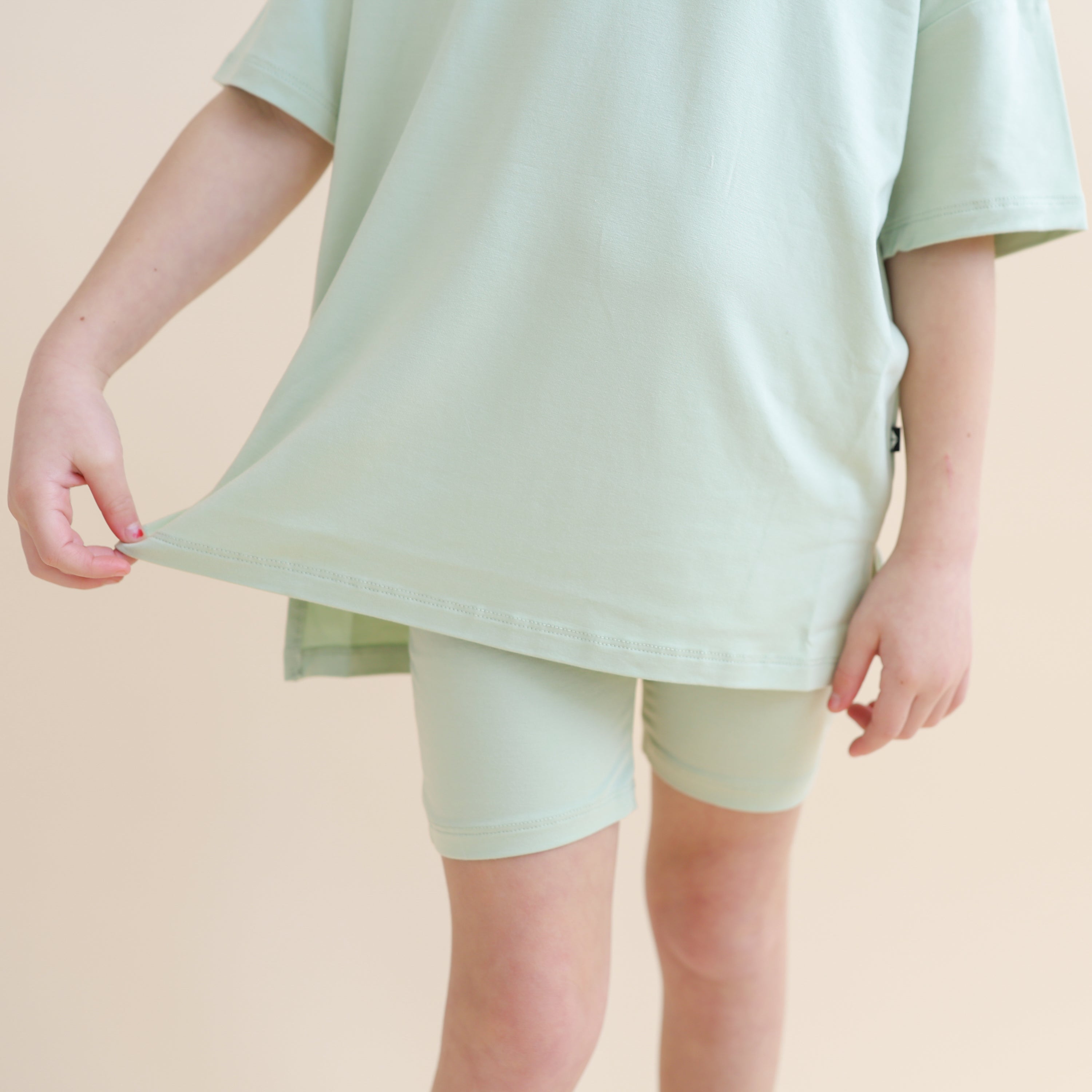 Close up of the hem on the shirt of the Toddler Biker Short Set in Basil shown on a model