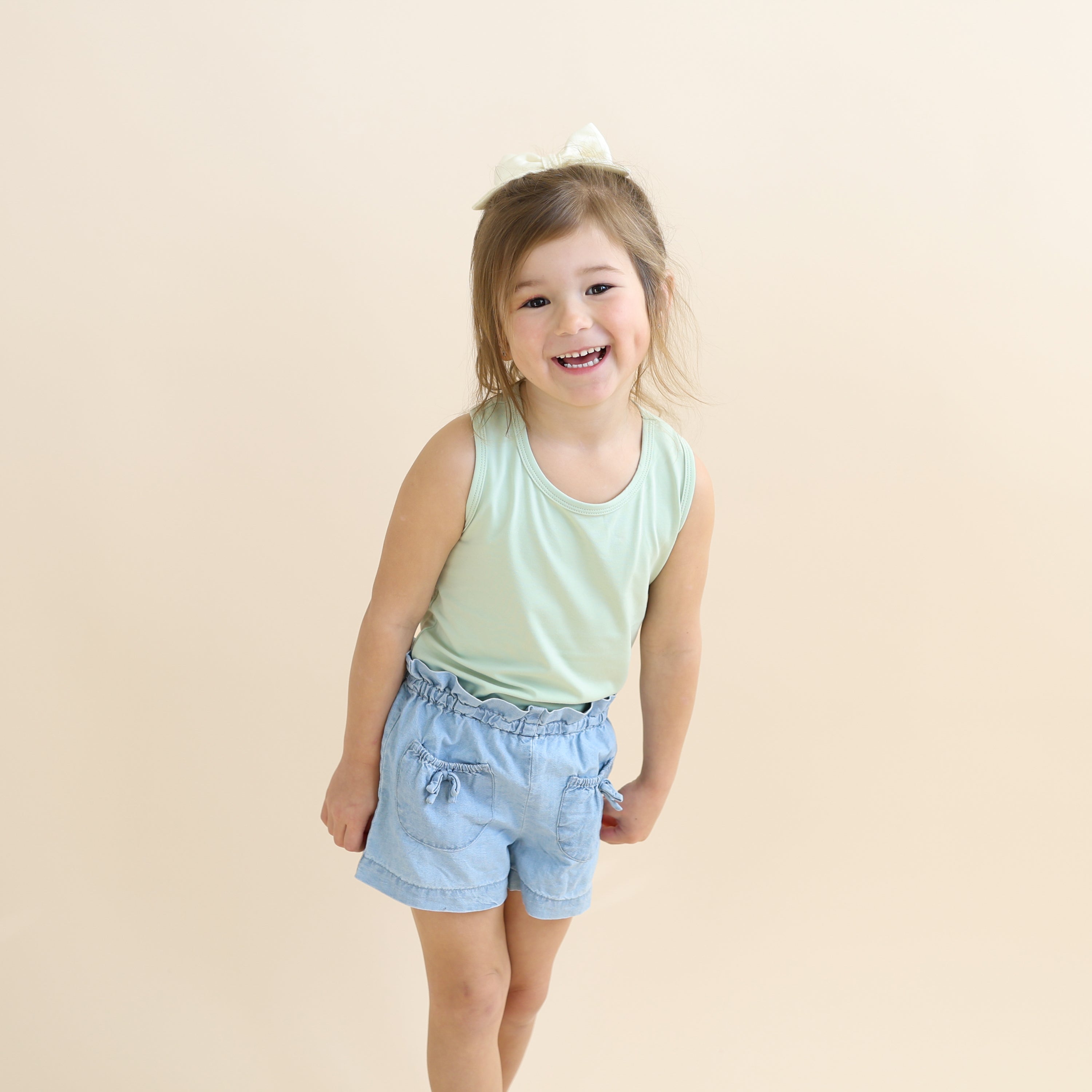 Young smiling girl wearing the Toddler Tank Top in Basil paired with jean shorts