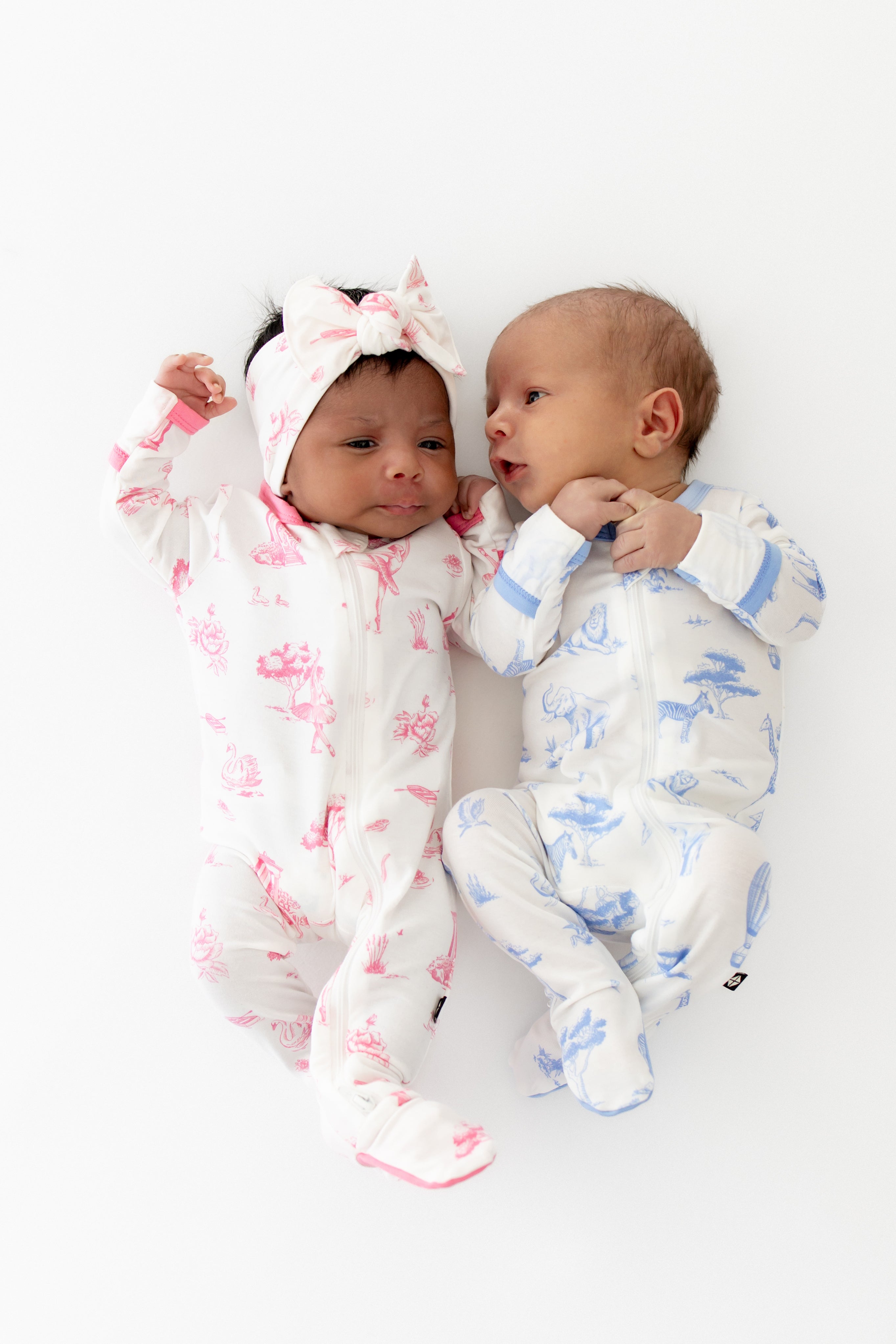 Two babies in colorful toile footed pajamas on a white background