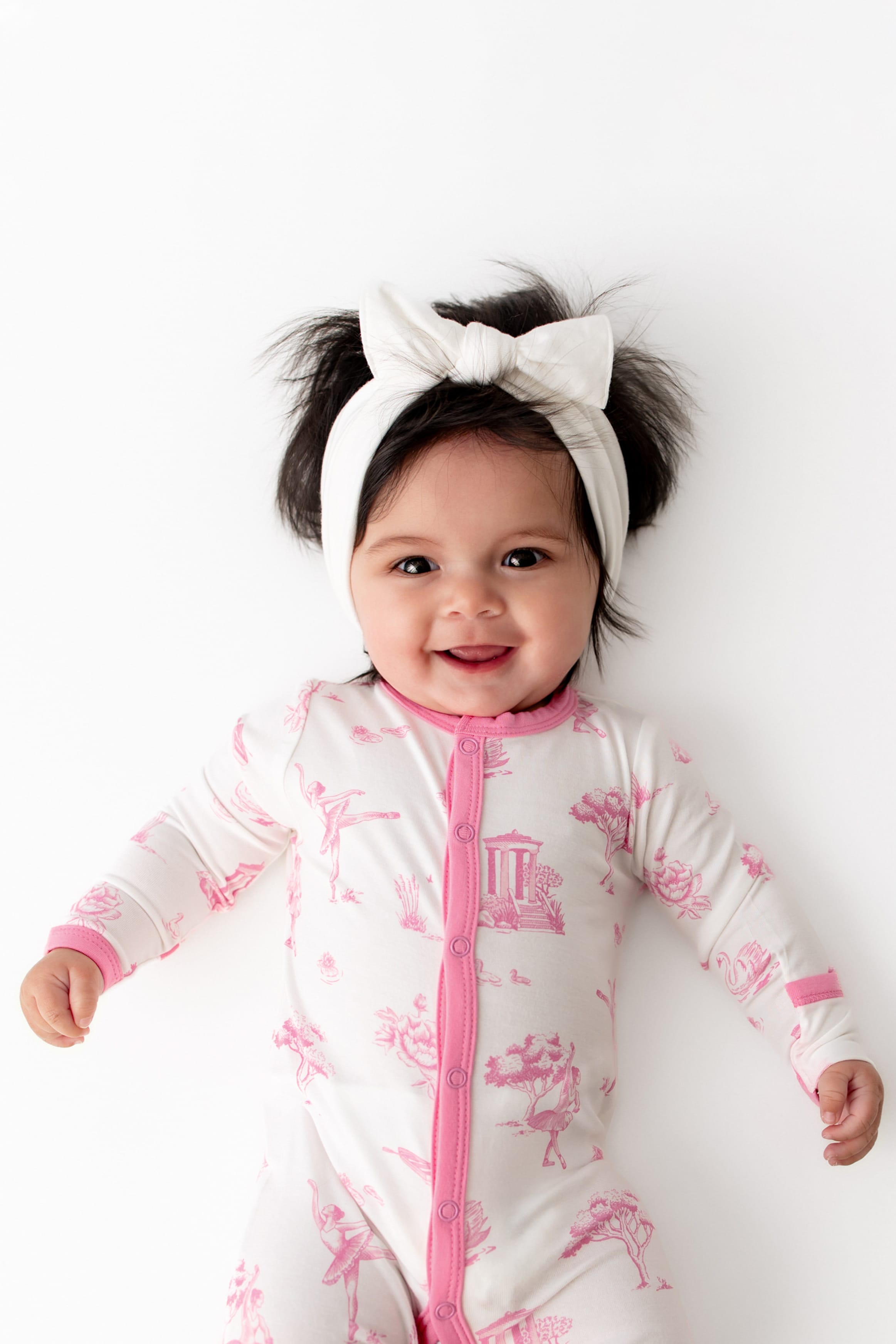 Close up of infant wearing the Romper in Toile Ballet paired with a white bow