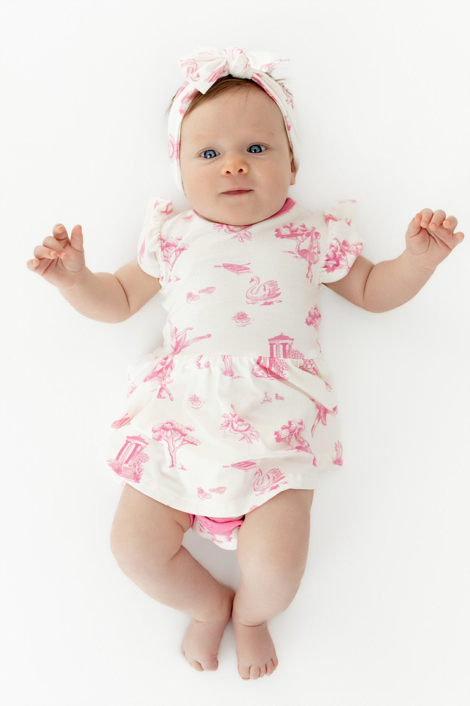 Close up of infant wearing the Twirl Bodysuit Dress in Toile Ballet with matching bow