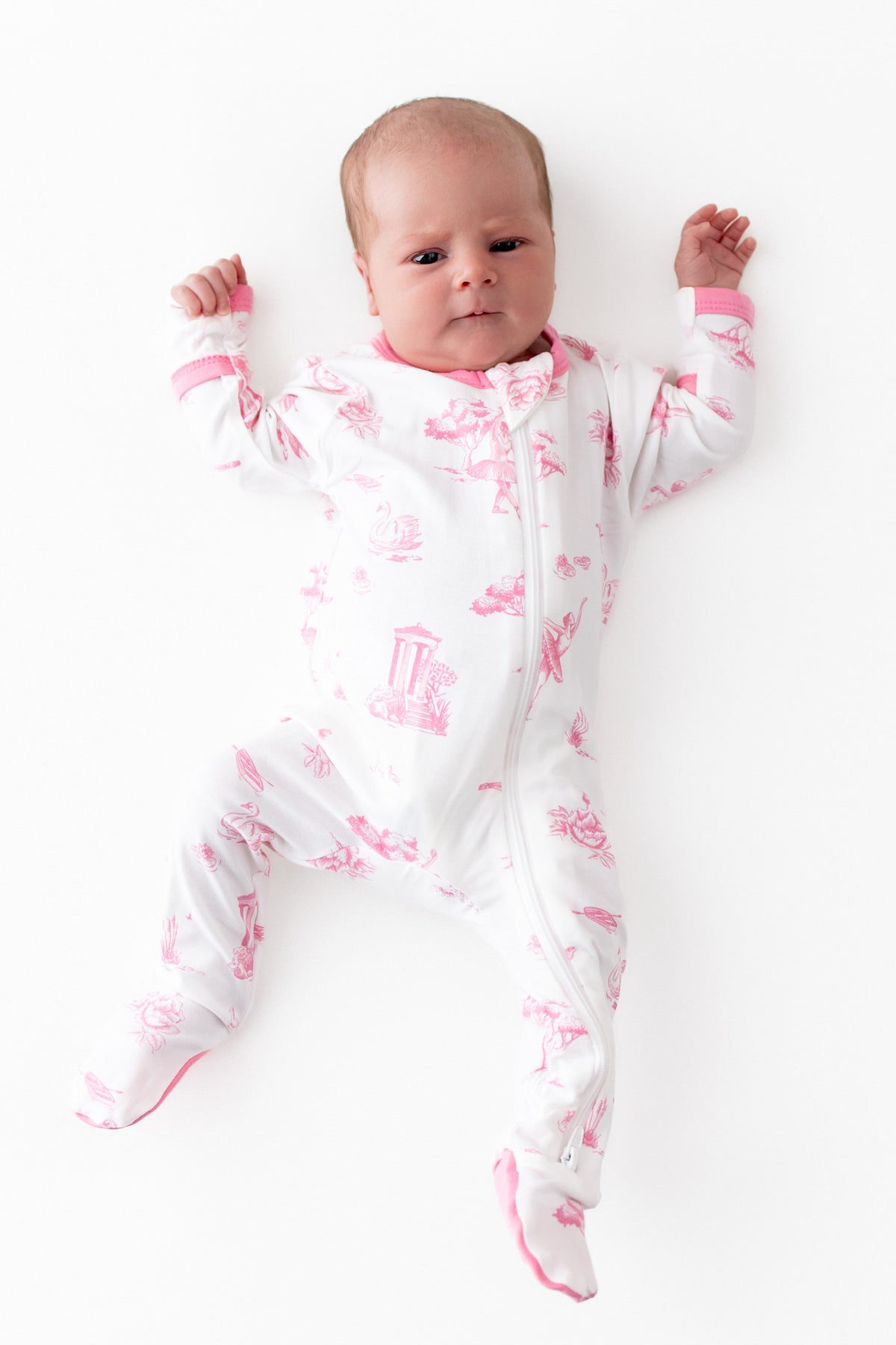 Newborn baby wearing the Zippered Footie in Toile Ballet laying on a white surface