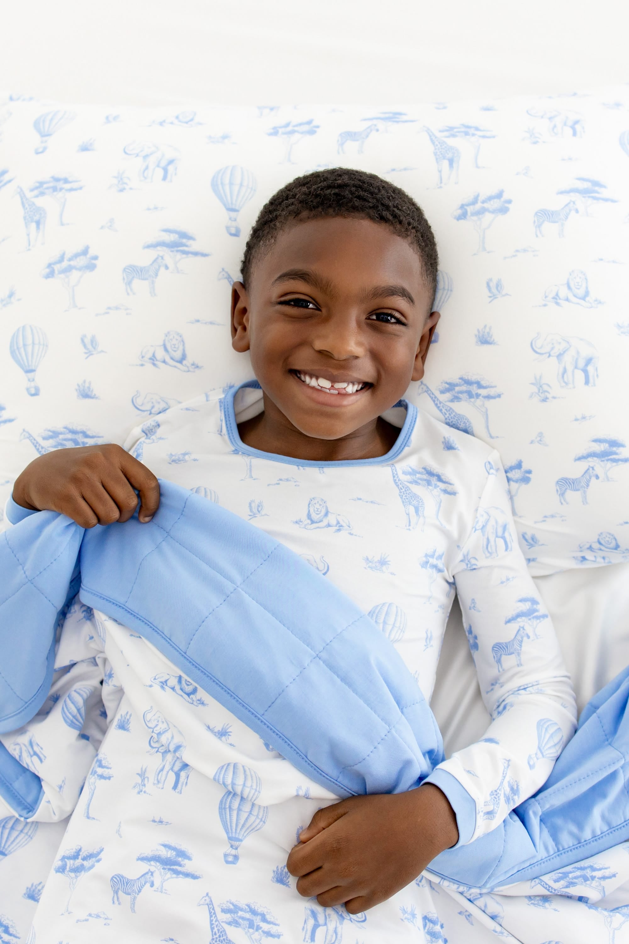 Young smiling boy laying on a Standard Pillowcase in Toile Safari with the matching blanket over top of him