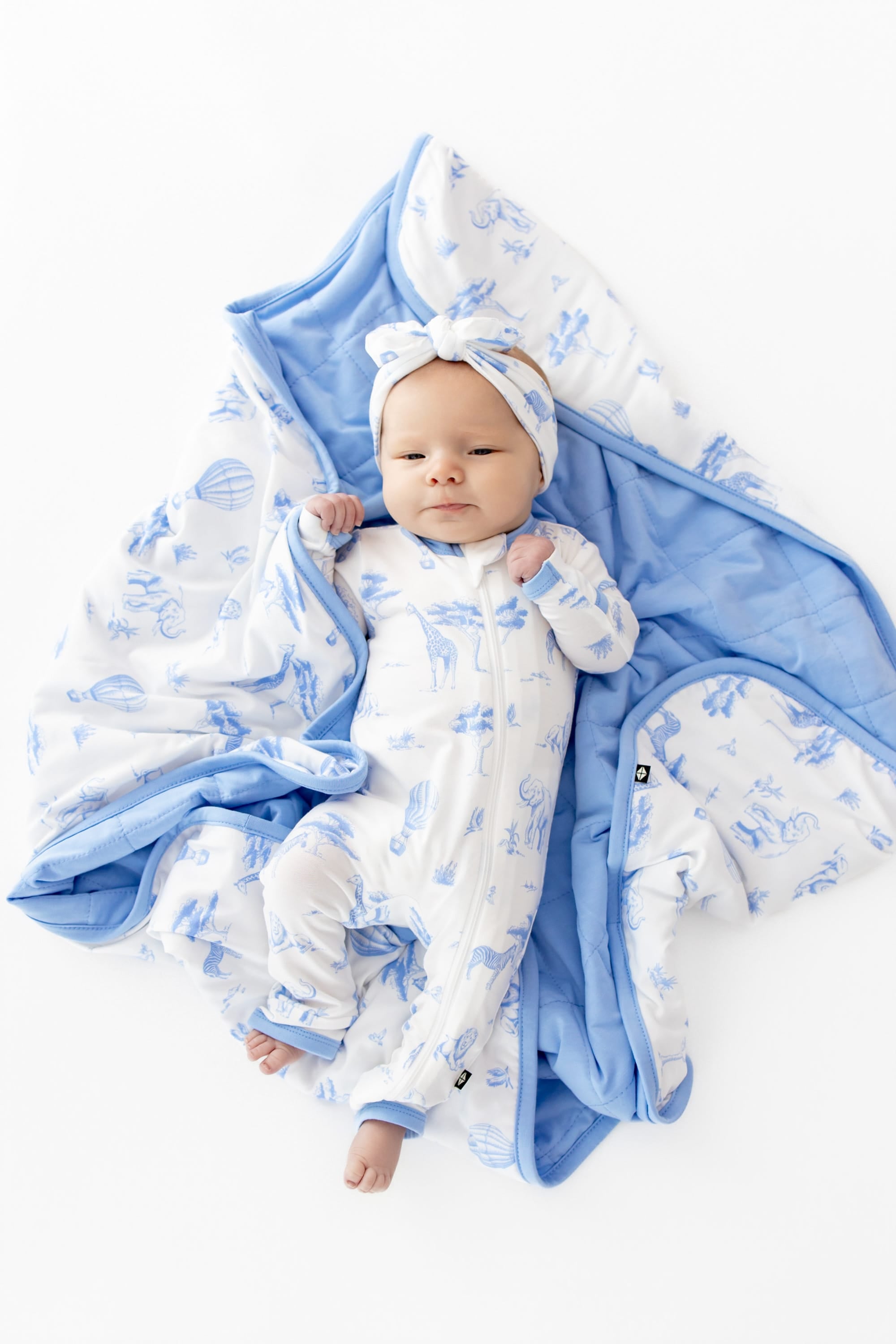 Infant girl laying on a Baby Blanket in Toile Safari wearing a matching zippered romper and bow