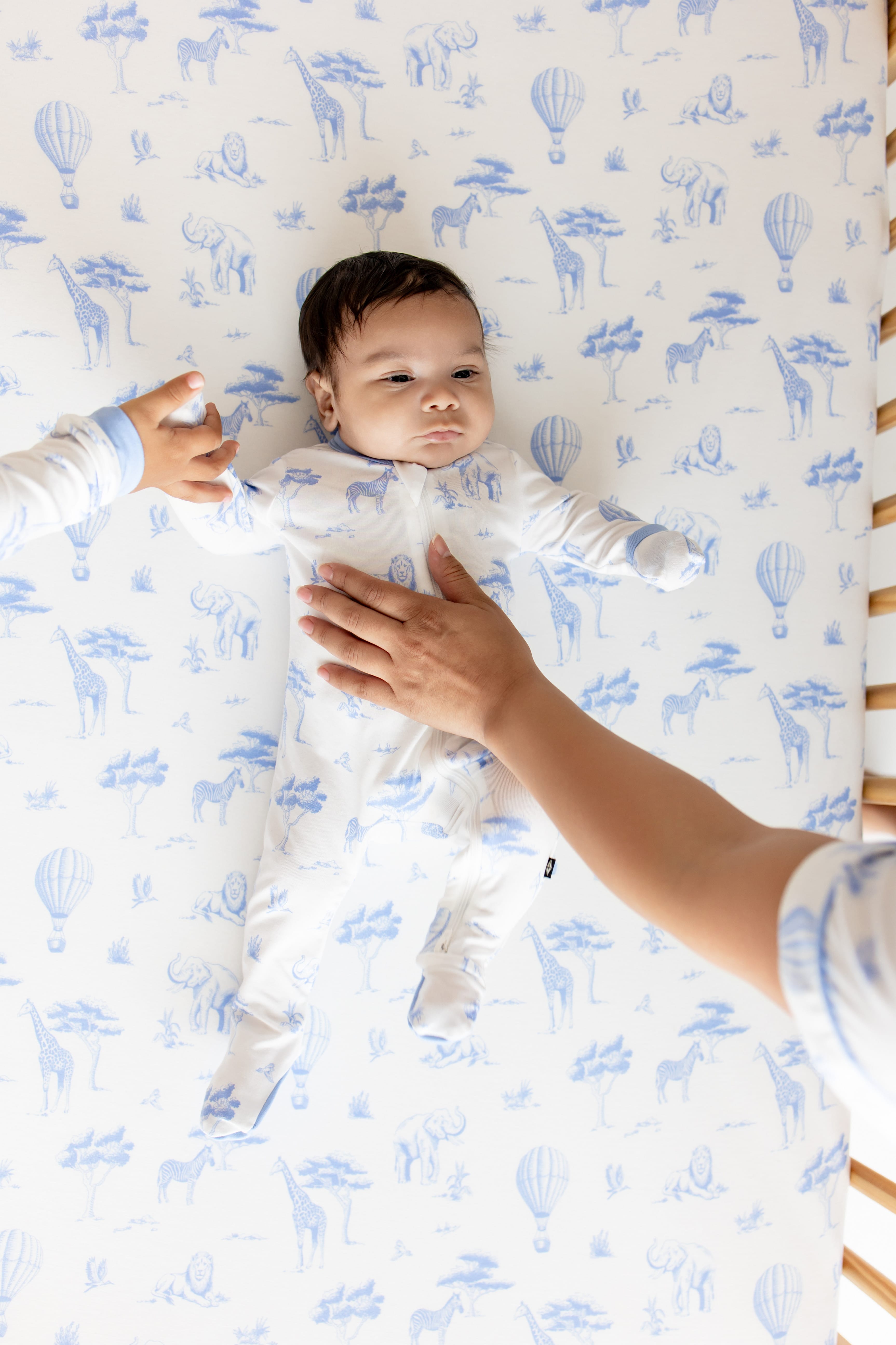 Infant laying in a crib on top of the Crib Sheet in Toile Safari wearing the matching zippered footie