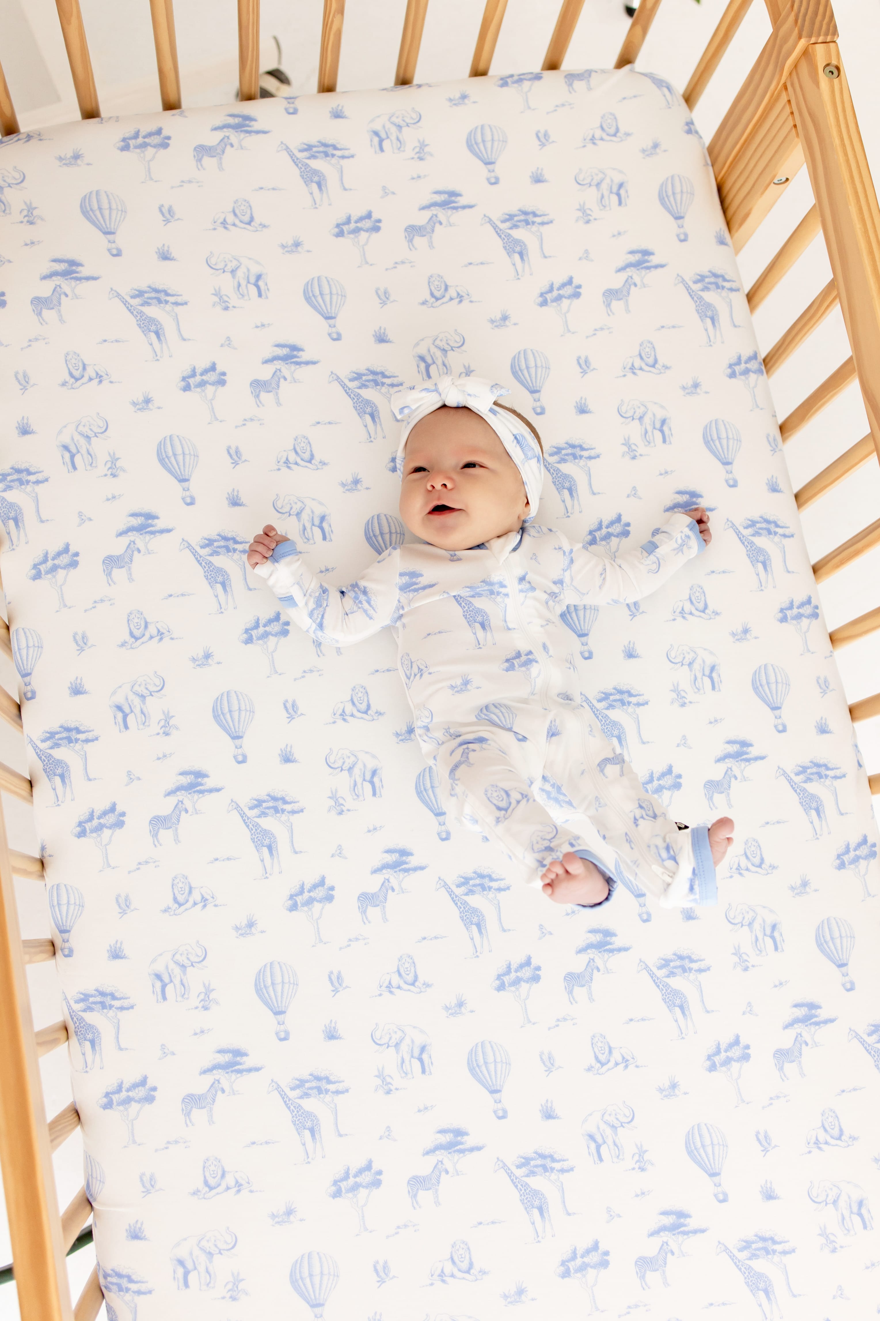 Infant wearing the Zippered Romper in Toile Safari on top laying in a crib on top of a matching crib sheet