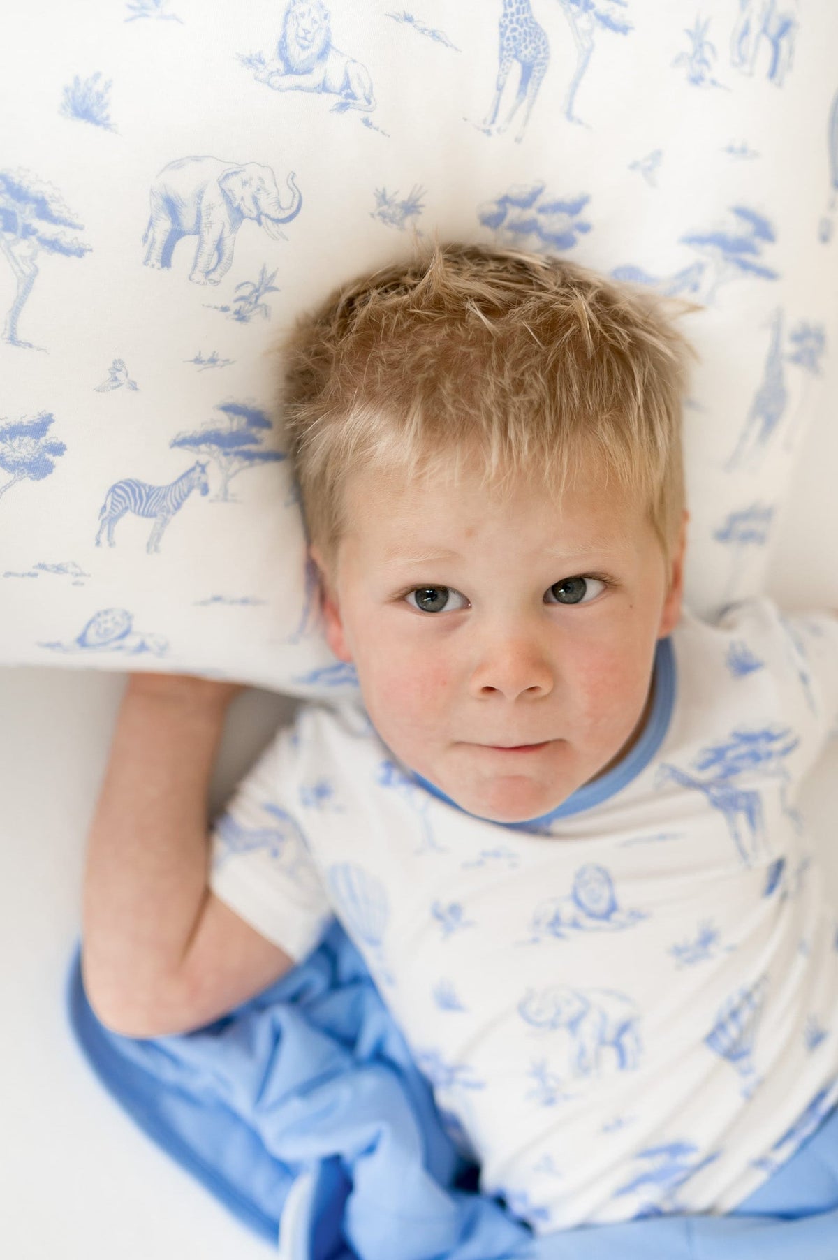 Young boy laying on a pillow with the Toddler Pillowcase in Toile Safari on it underneath a matching blanket