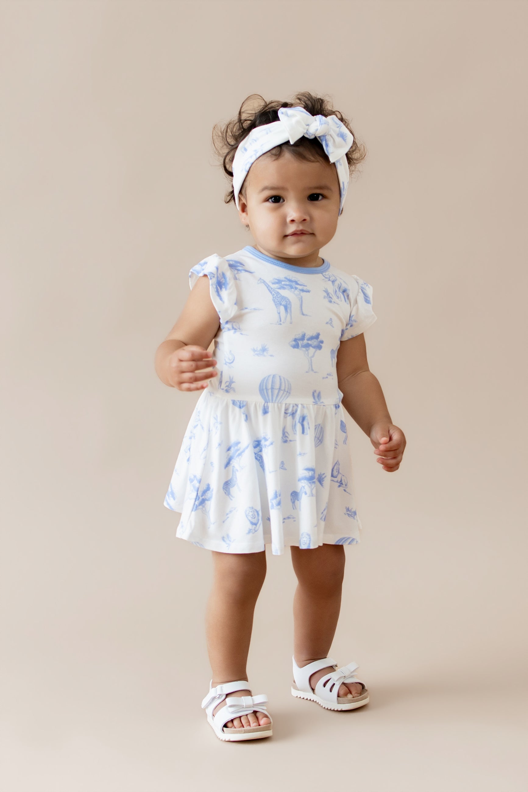 Young toddler standing wearing the Twirl Bodysuit Dress in Toile Safari