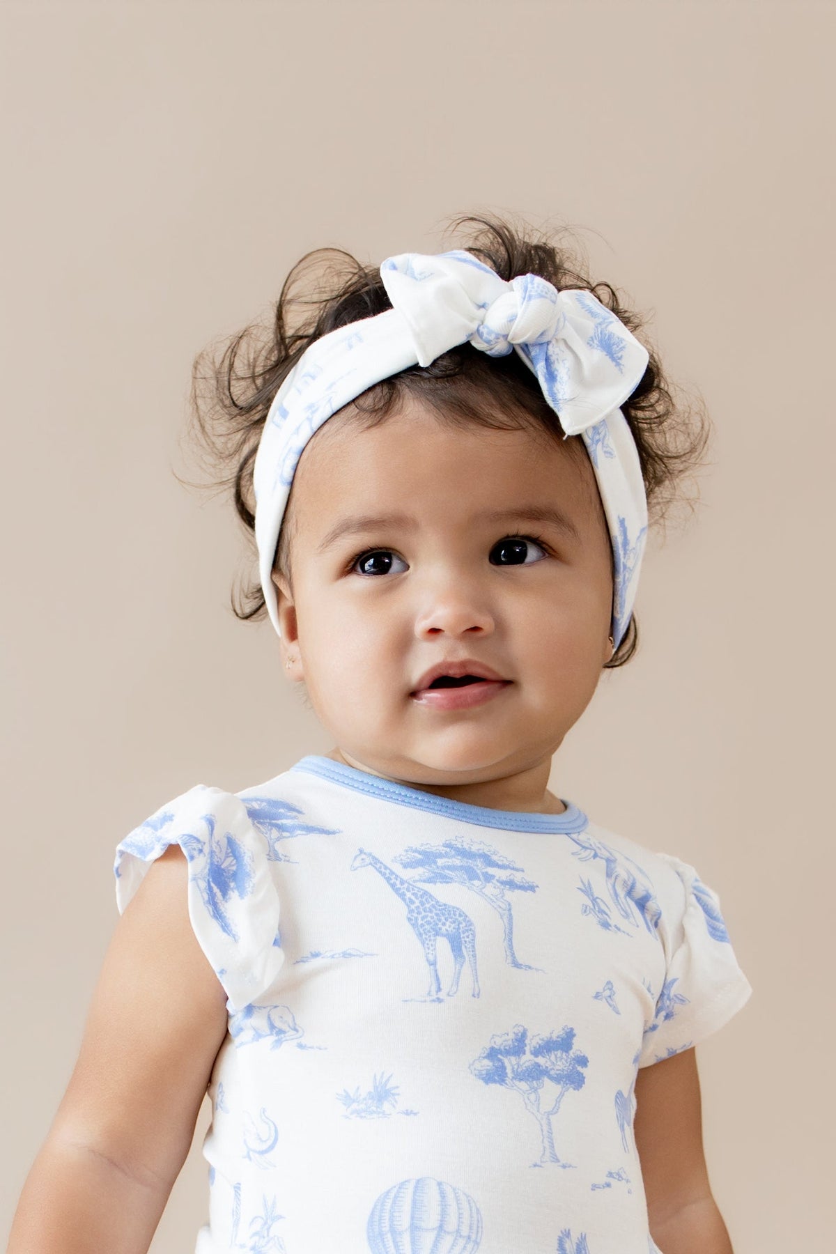 Close up of young girl wearing the Knotted Bow Headband in Toile Safari with matching twirl bodysuit dress
