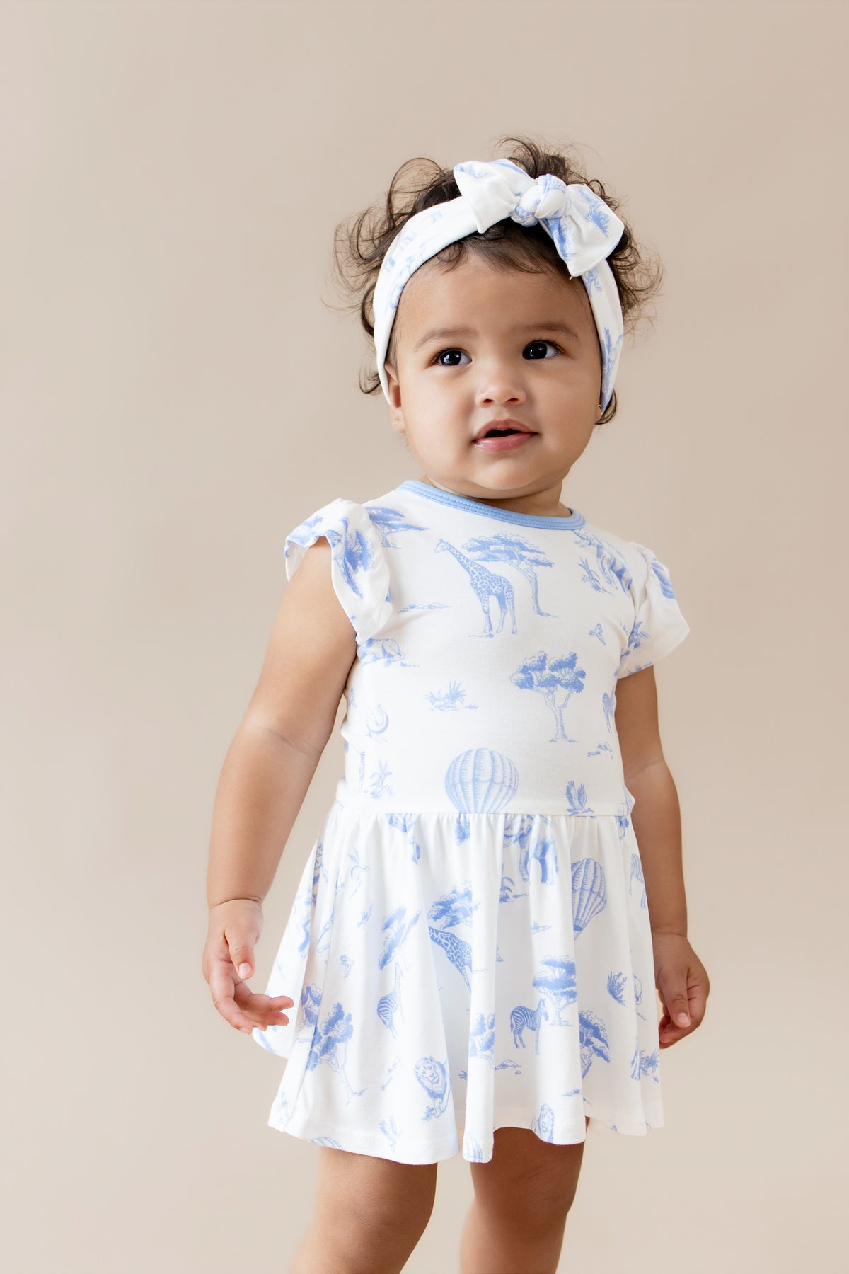 Close up of toddler wearing the Twirl Bodysuit Dress in Toile Safari with matching bow