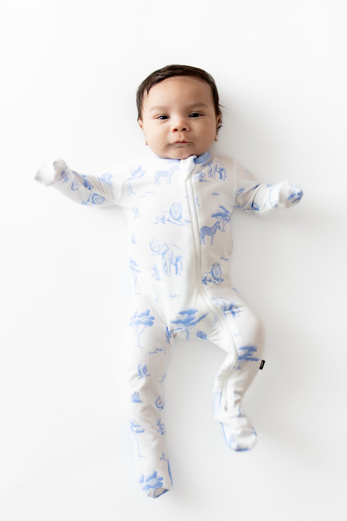 Newborn infant wearing the Zippered Footie in Toile Safari with the hand cuffs folded over his hands