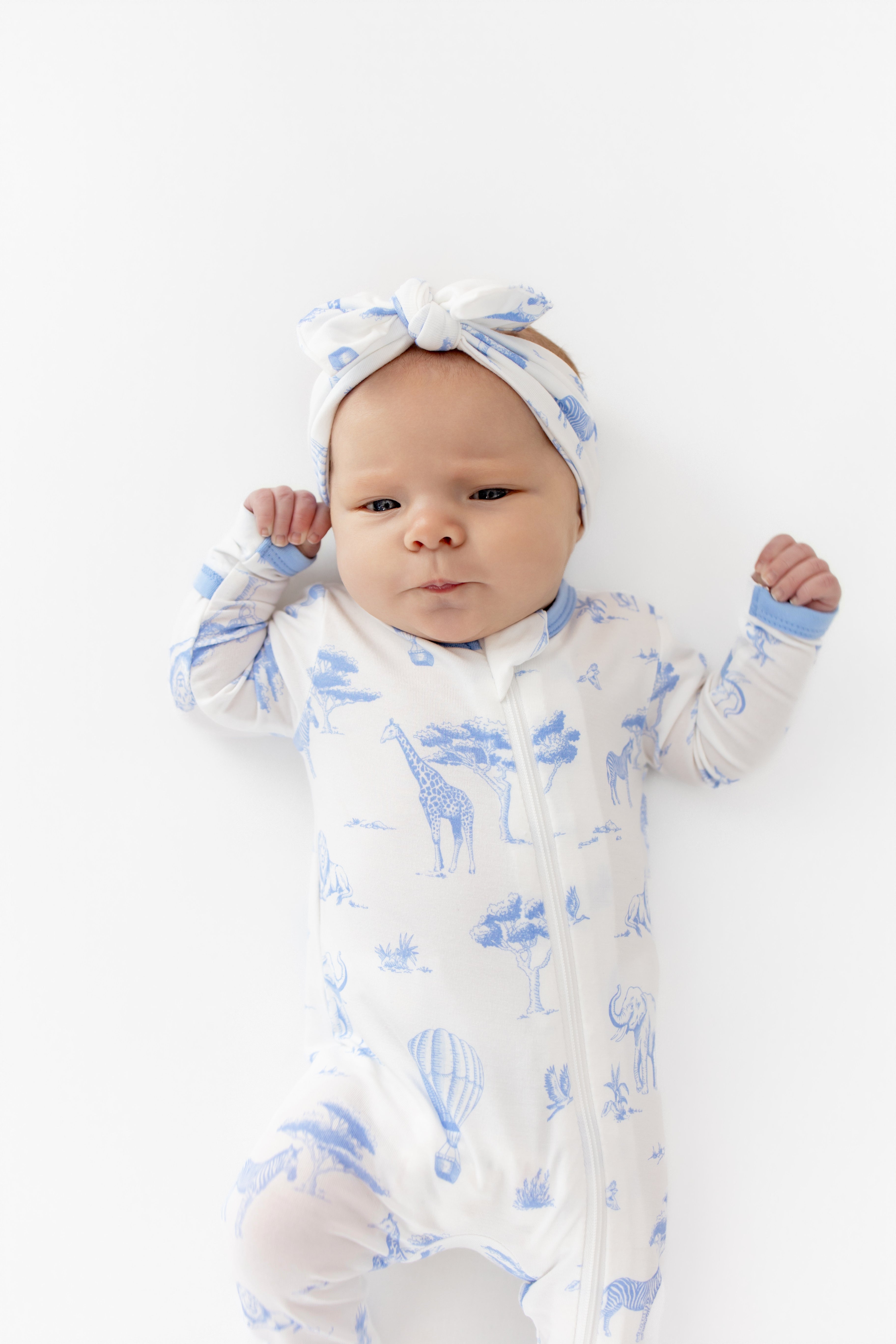 Close up of newborn wearing the Zippered Romper in Toile Safari paired with a matching bow