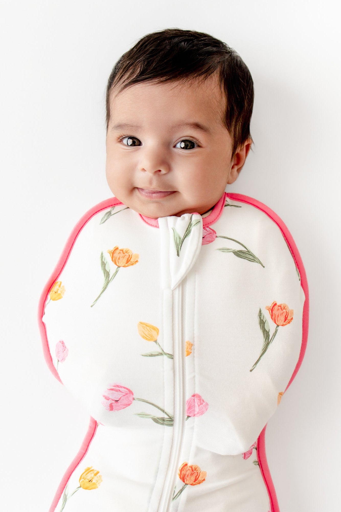 Close up of newborn wearing the Swaddle Bag in Tulip 0.5 laying on a white surface
