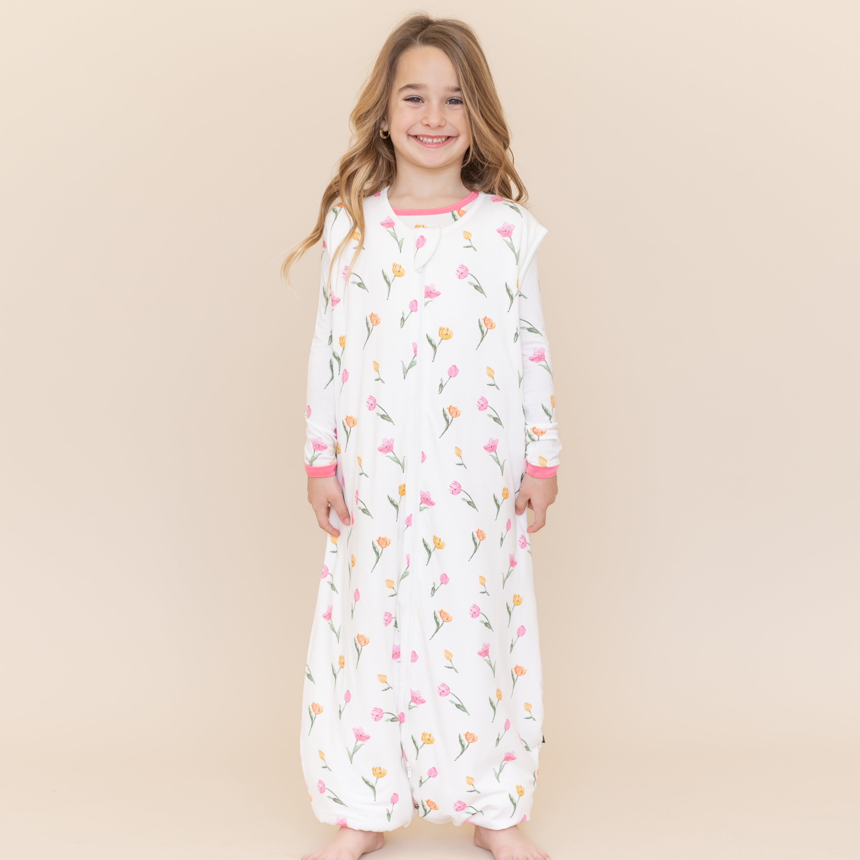 Young smiling girl modeling the Sleep Bag Walker in Tulip 1.0 with matching long sleeve pajamas on underneath