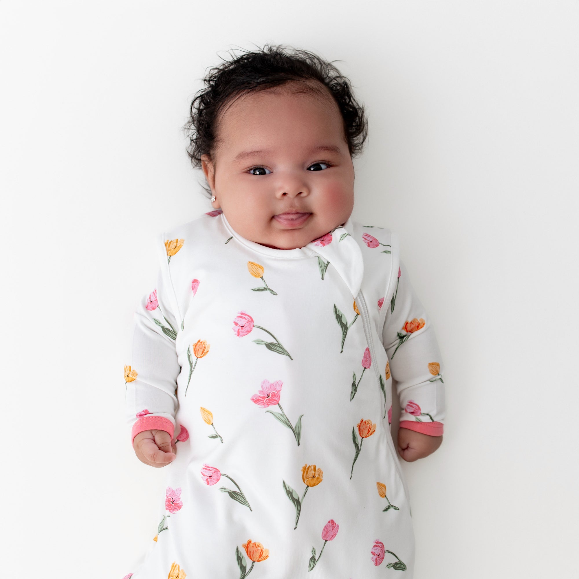 Close up infant wearing the Sleep Bag in Tulip 1.0 with a matching romper on underneath
