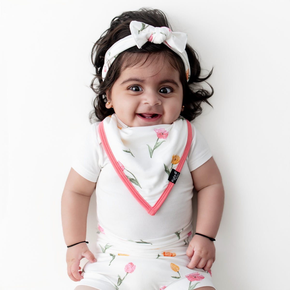 Young infant wearing the Bib in Tulip with matching bummies and headband and white short sleeve bodysuit