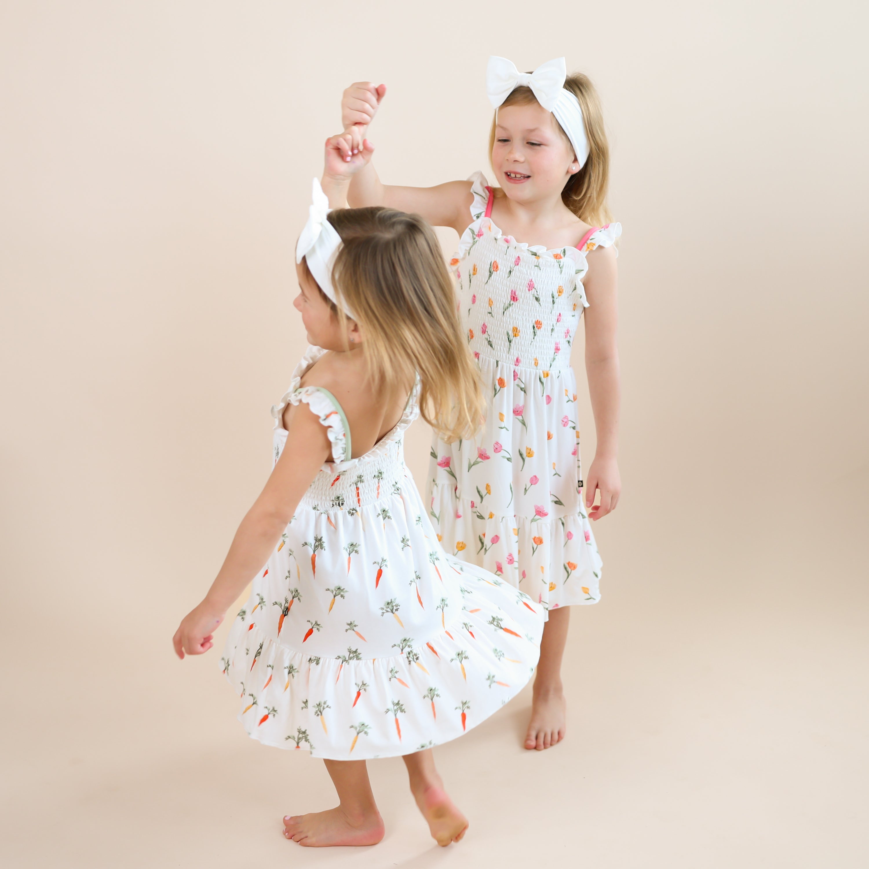 Two sisters holding hands twirling wearing the Smocked Dress in Carrot and Tulip