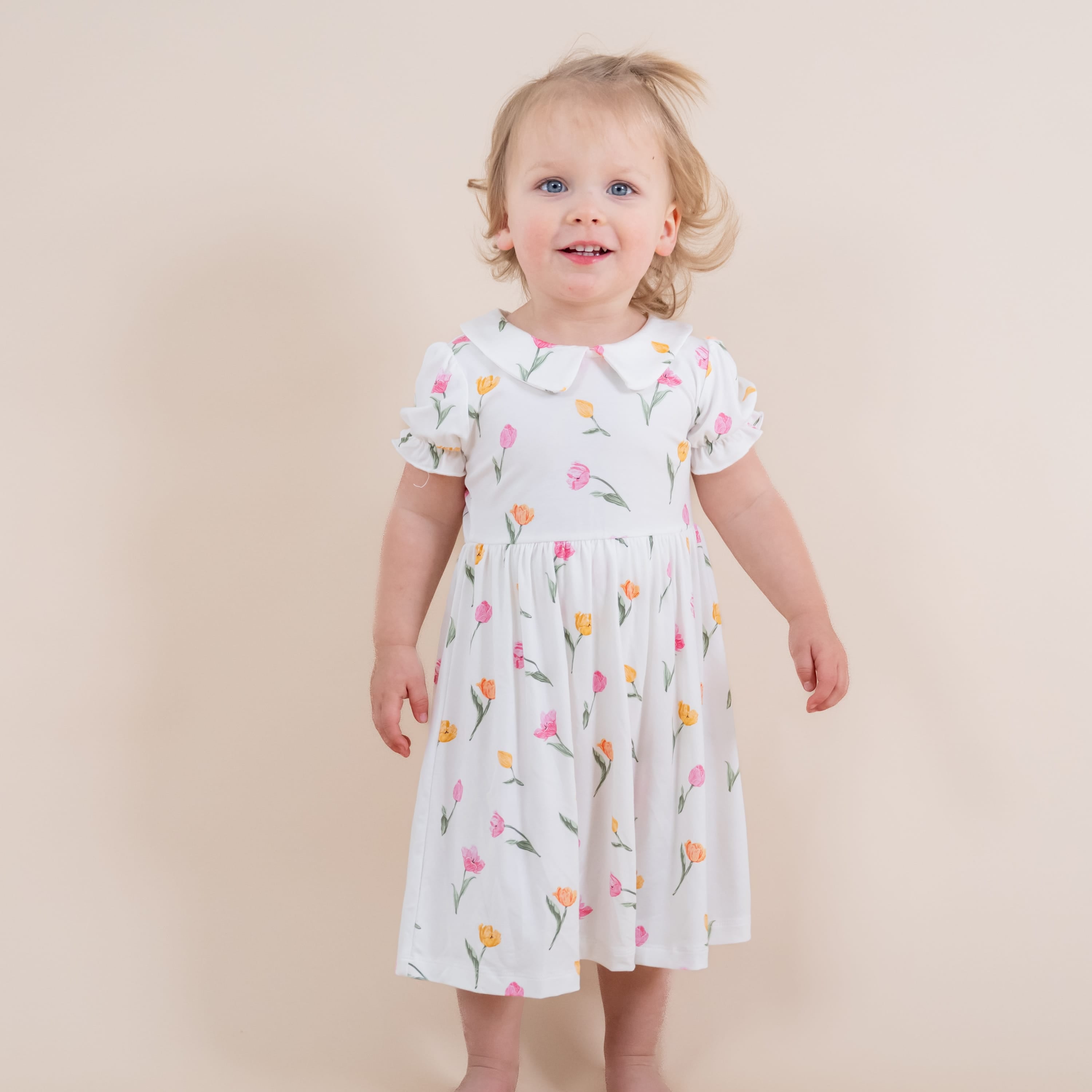 Young girl modeling the Peter Pan Collar Bodysuit Dress in Tulip standing in front of a light neutral background