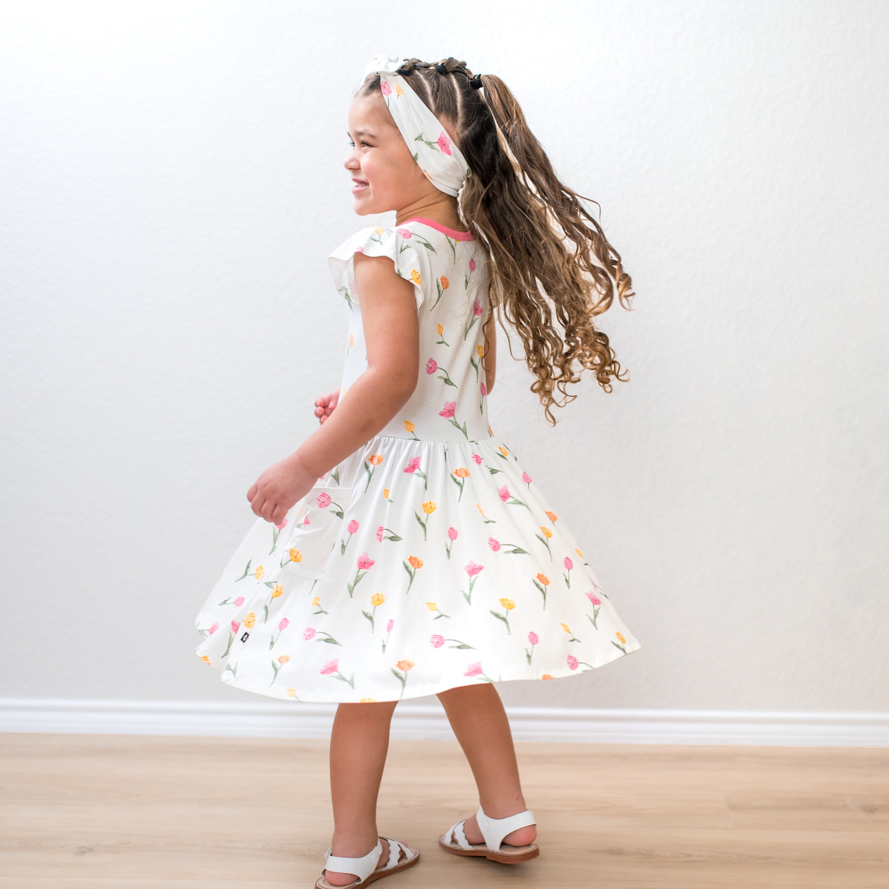 Young girl twirling wearing the Pocket Dress in Tulip with matching bow headband