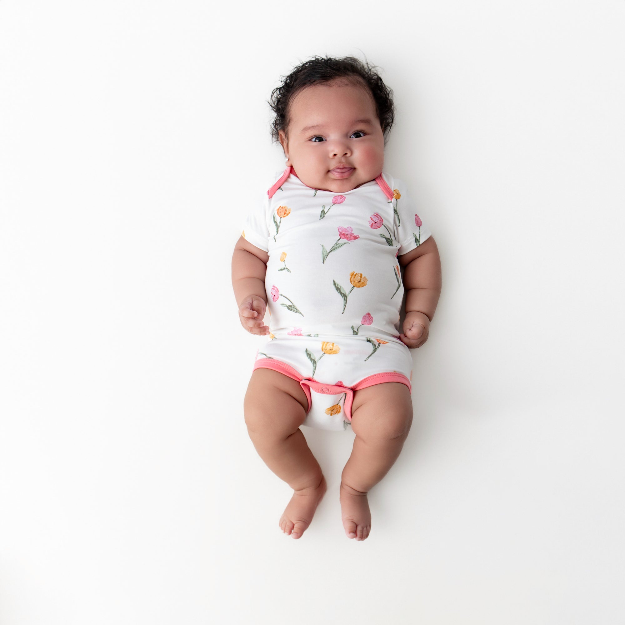 Newborn laying on a white surface wearing the Bodysuit in Tulip