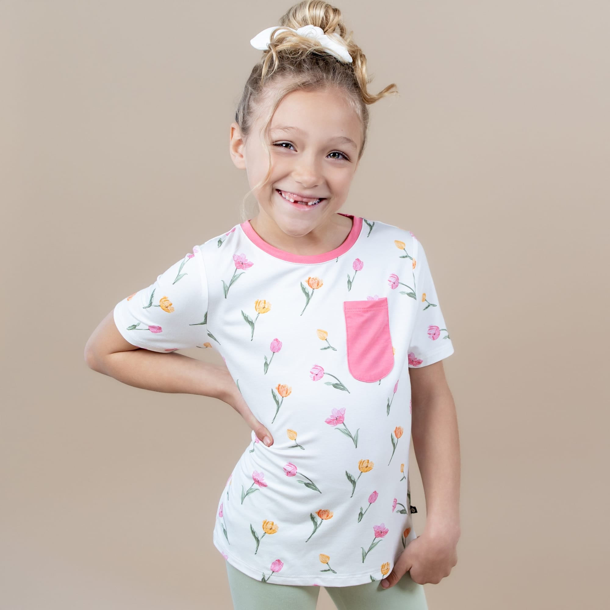 Young girl modeling the Toddler Crew Neck Tee in Tulip standing in front of a light taupe background
