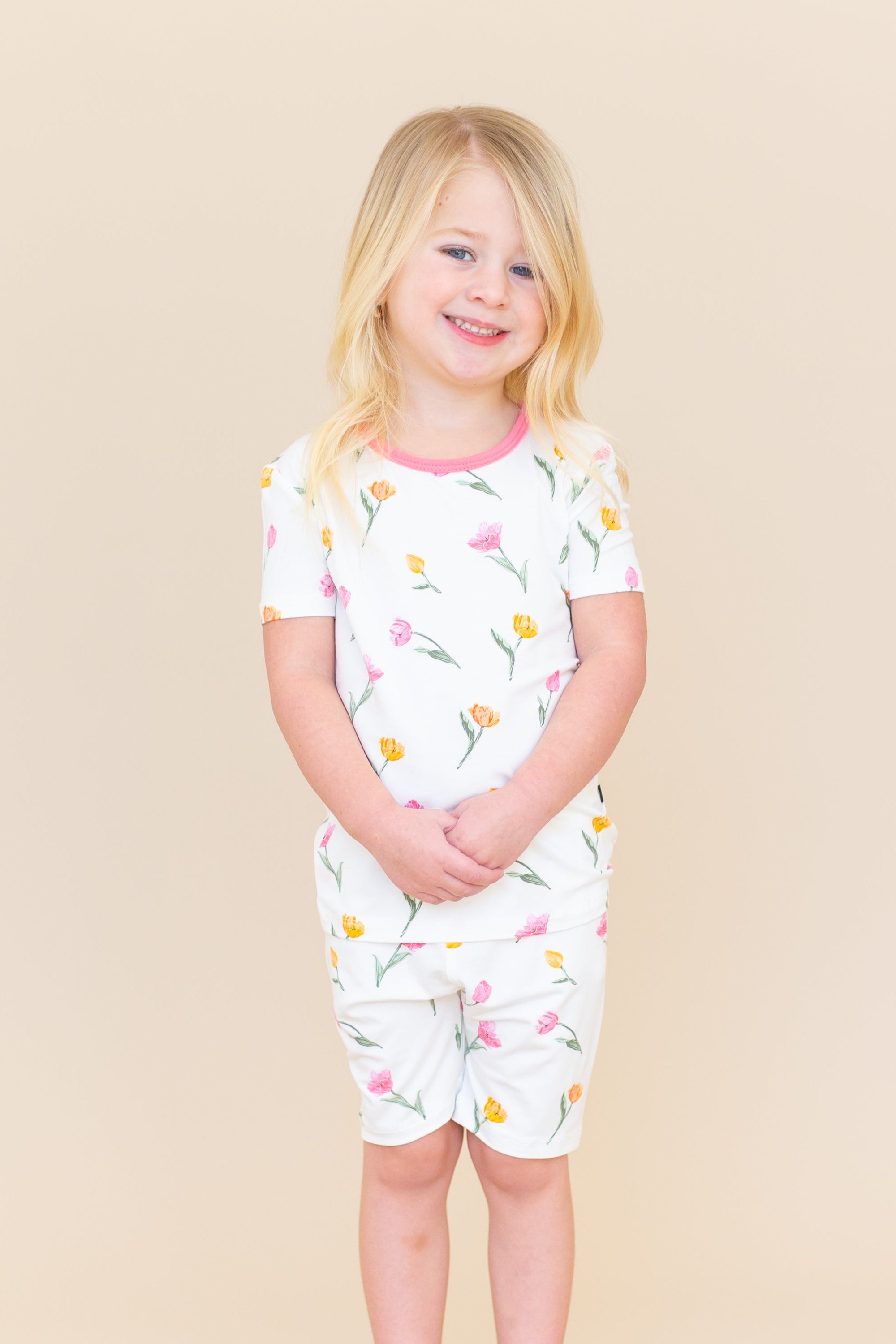 Young girl standing in front of a light taupe background wearing the Short Sleeve Pajamas in Tulip with her hands folded in front of her