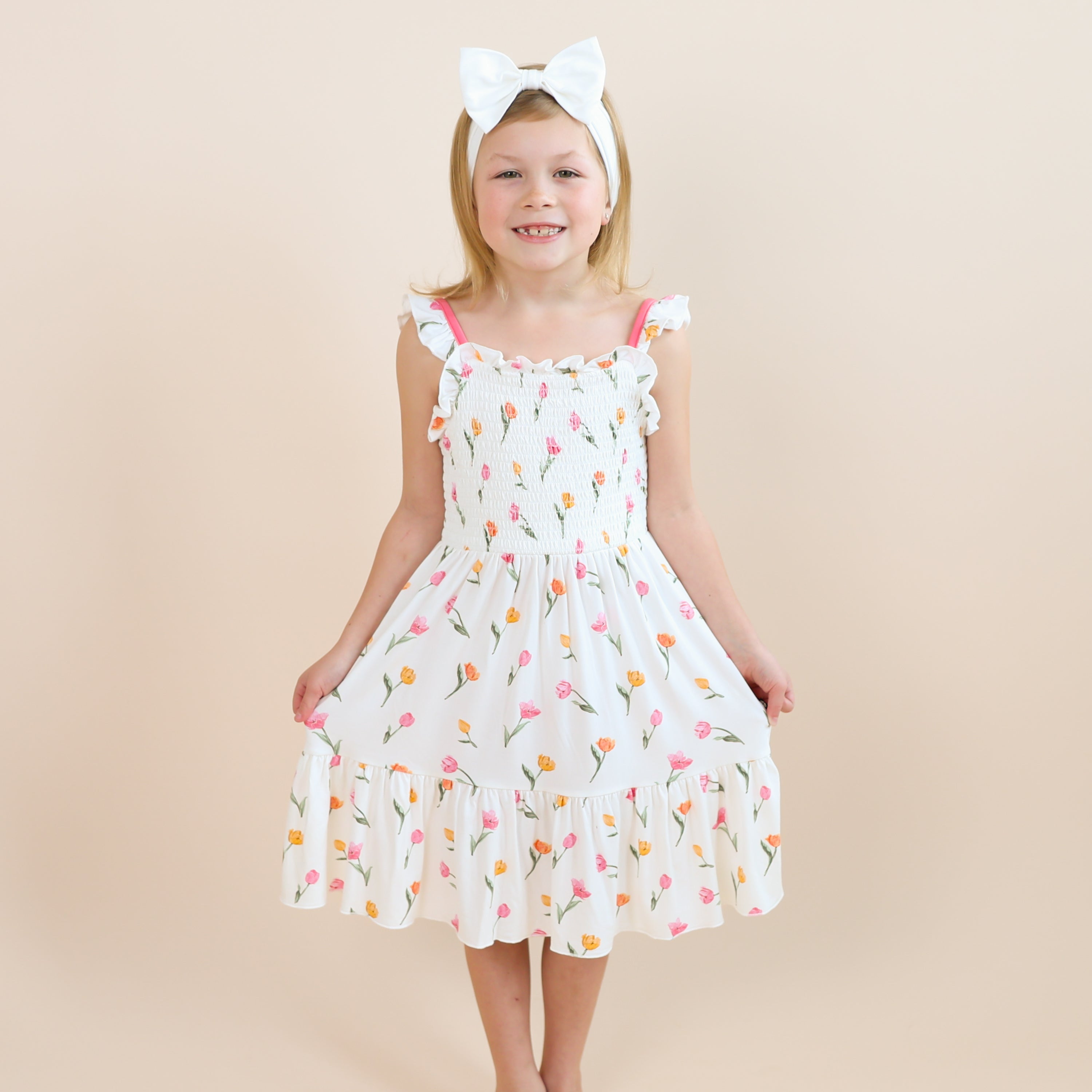 Smiling girl modeling the Smocked Dress in Tulip with a white bow headband