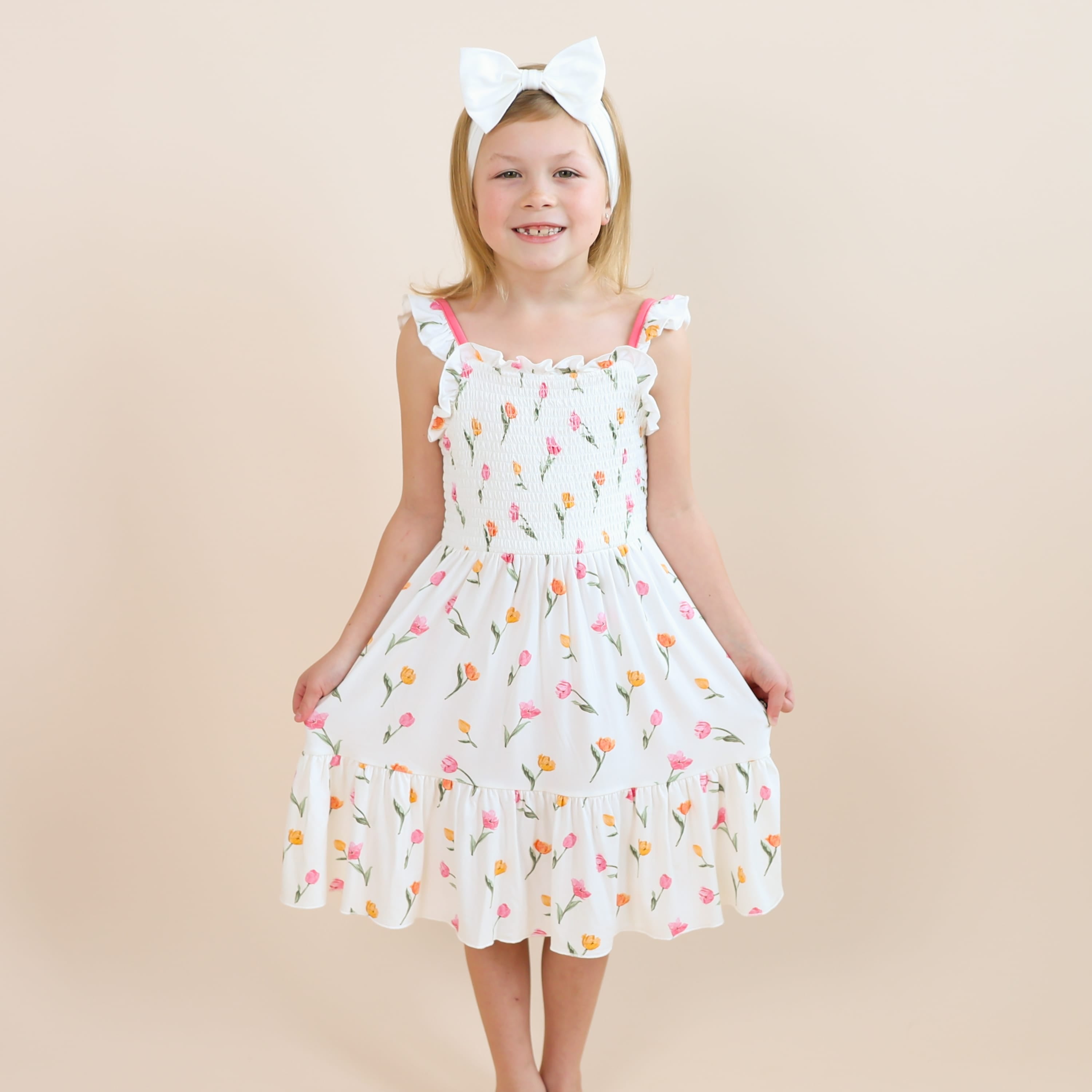 Smiling girl modeling the Smocked Dress in Tulip with a white bow headband