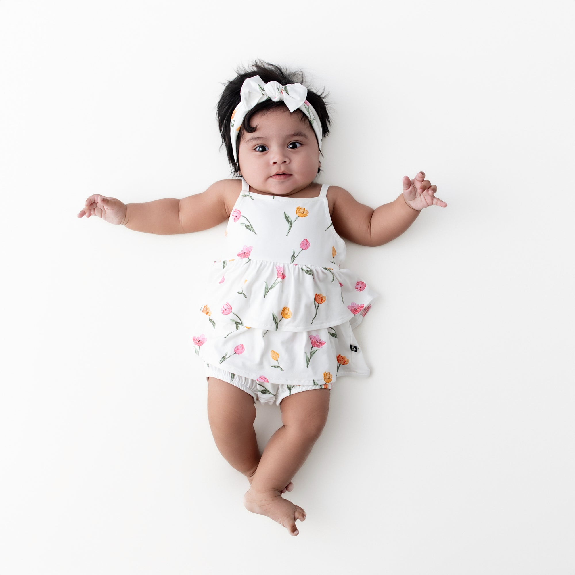 Infant wearing the Spaghetti Strap Ruffle Romper in Tulip with knotted bow headband
