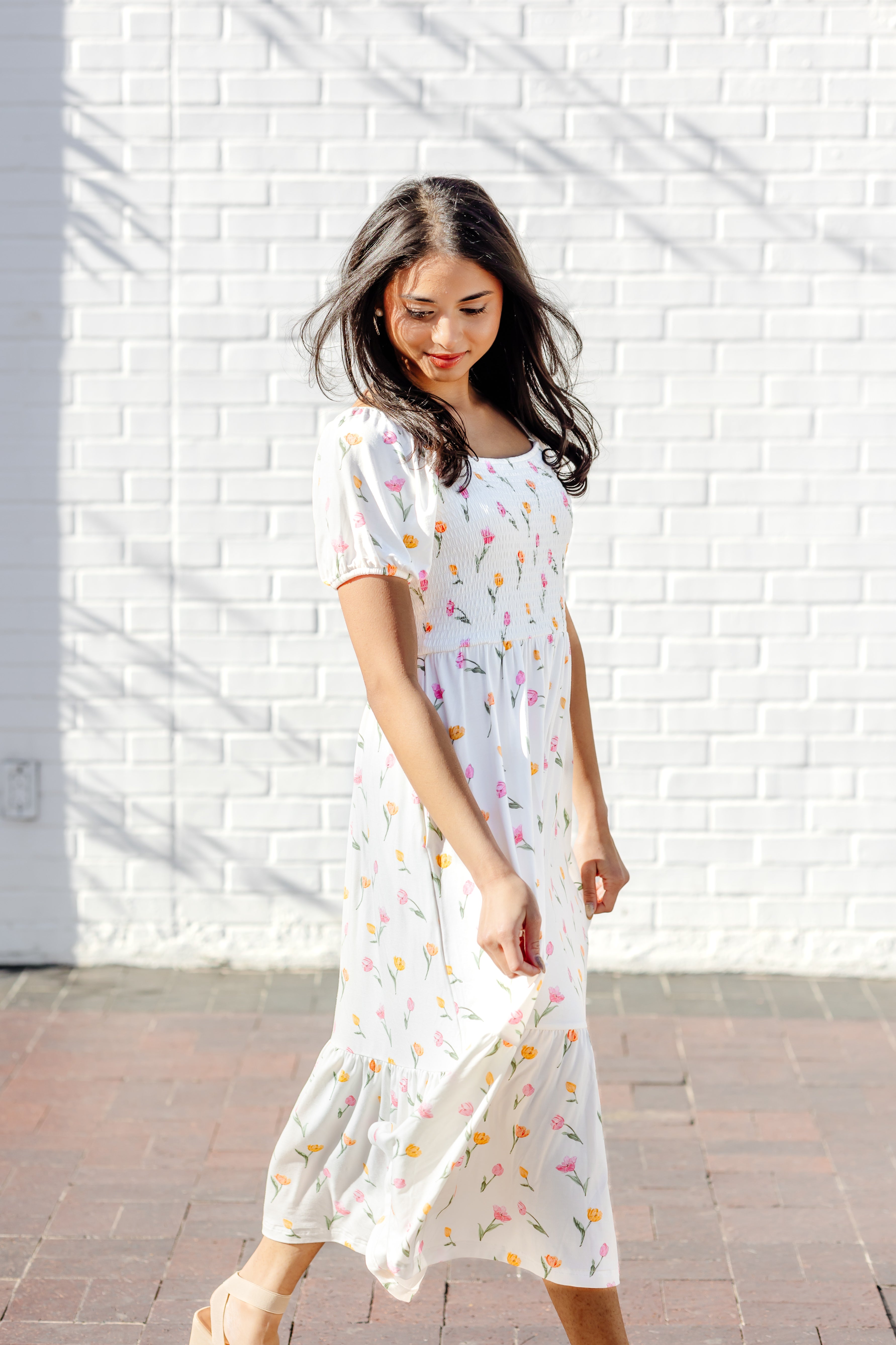 Female walking in front of a white brick wall wearing the Women’s Smocked Dress in Tulip