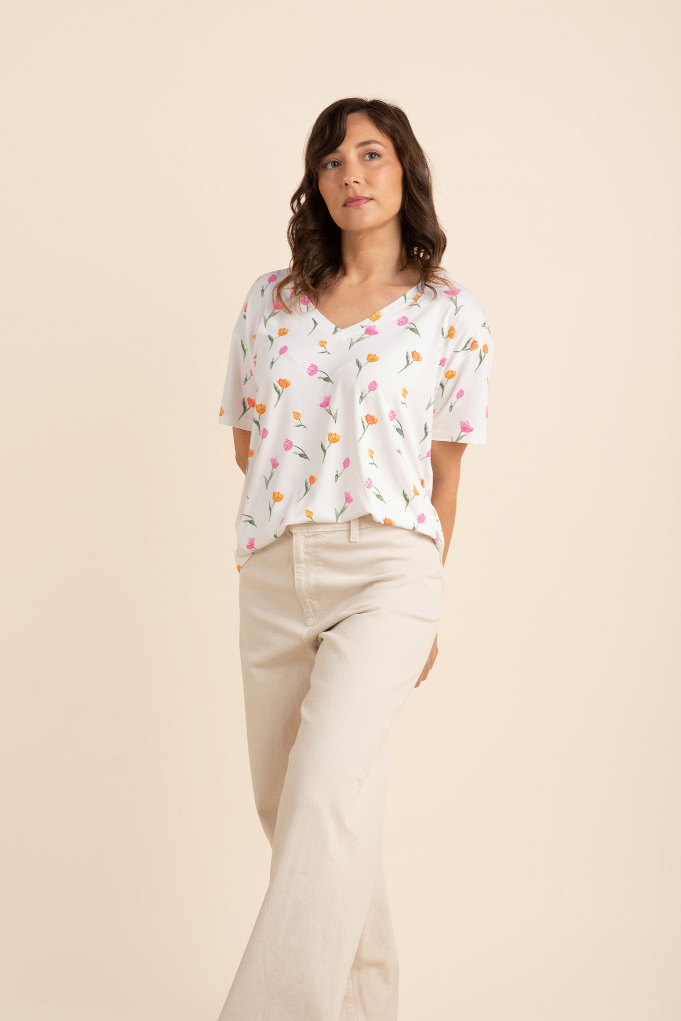 Female posing in front of a light beige background wearing the Women's Relaxed Fit V-Neck in Tulip with cream pants