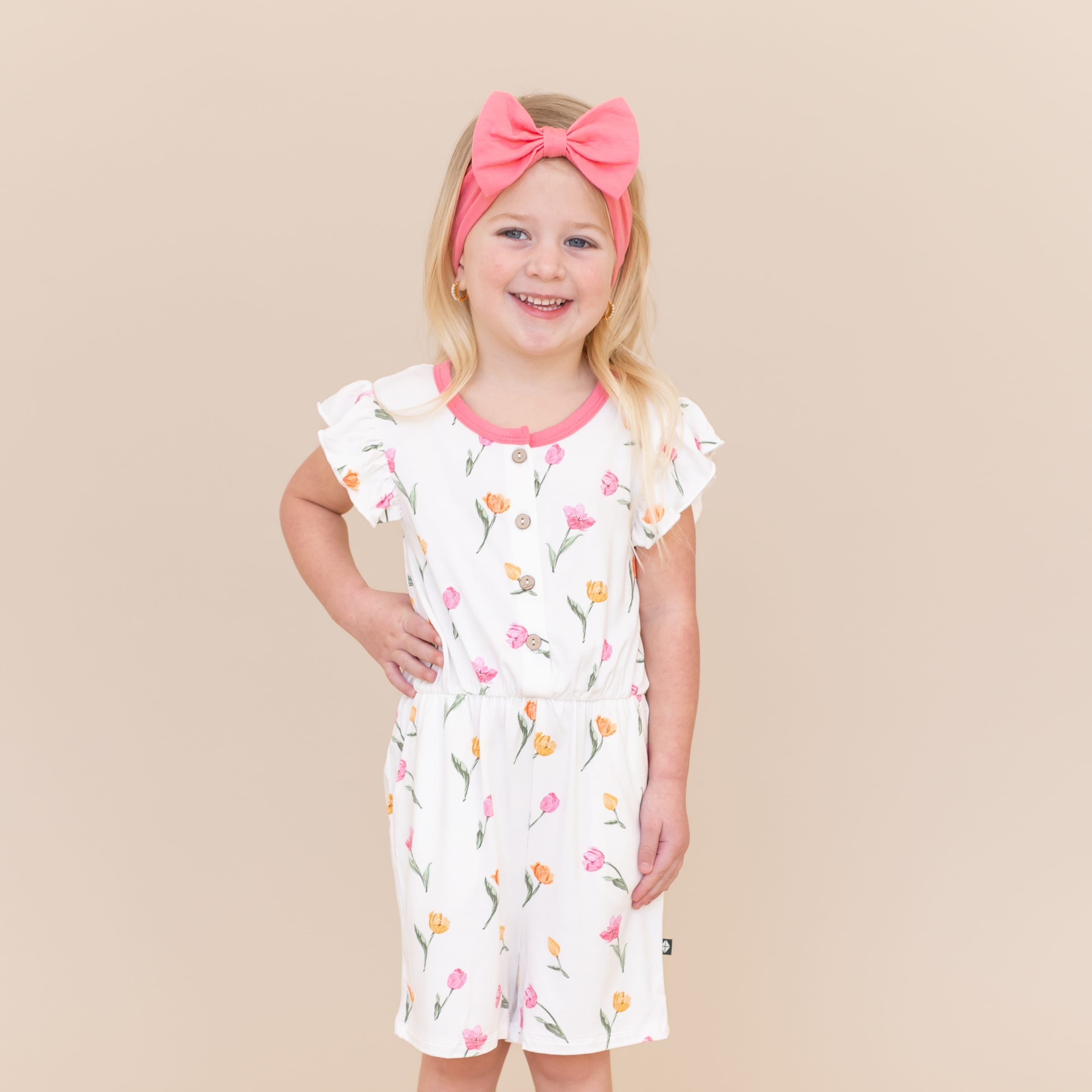Young girl posing wearing the Flutter Sleeve Romper in Tulip in front of a light neutral surface