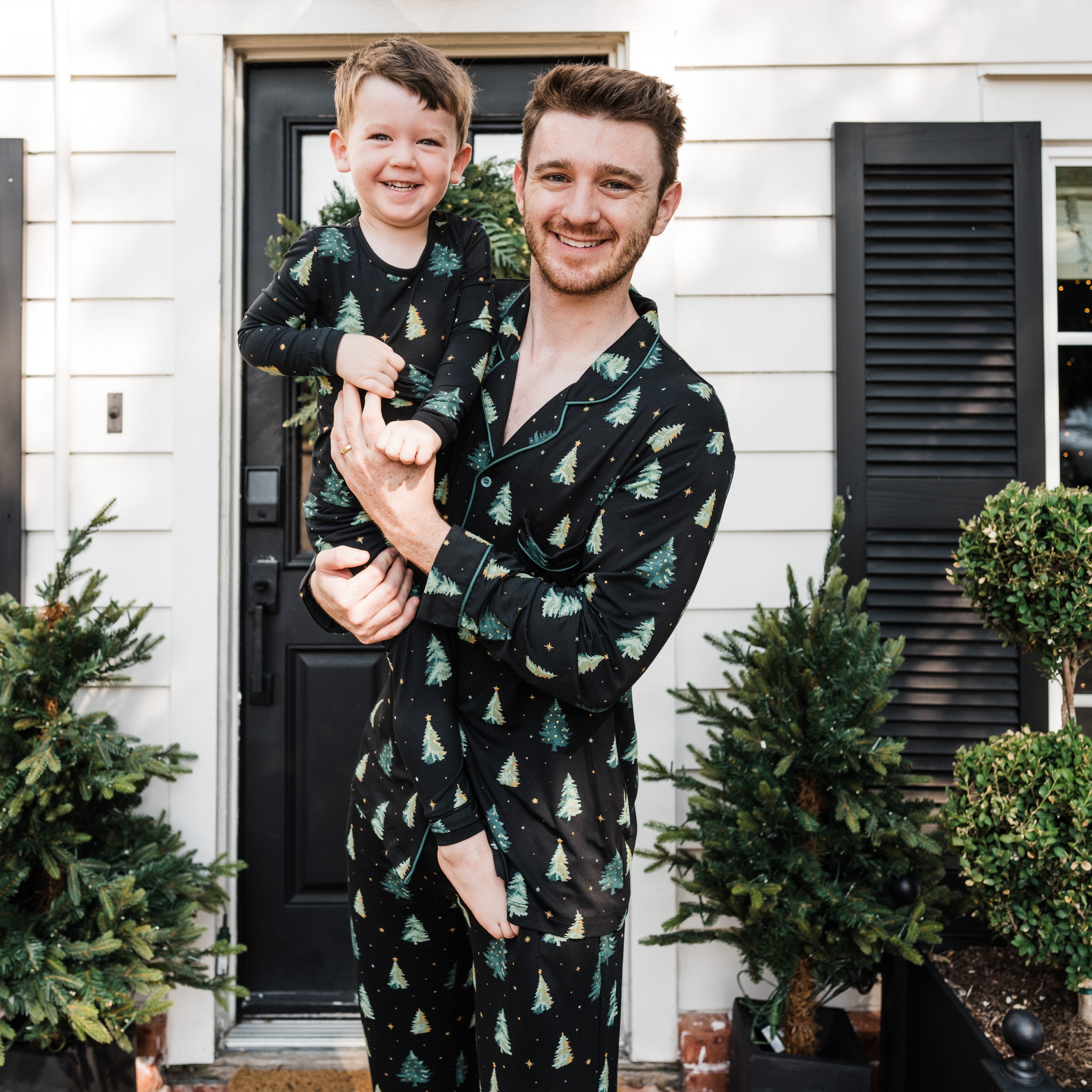 Father holding son both matching in Twinkle Tree. Father wearing the Men's Long Sleeve Pajama Set in Twinkle Tree and young boy is wearing the toddler long sleeve pajama set