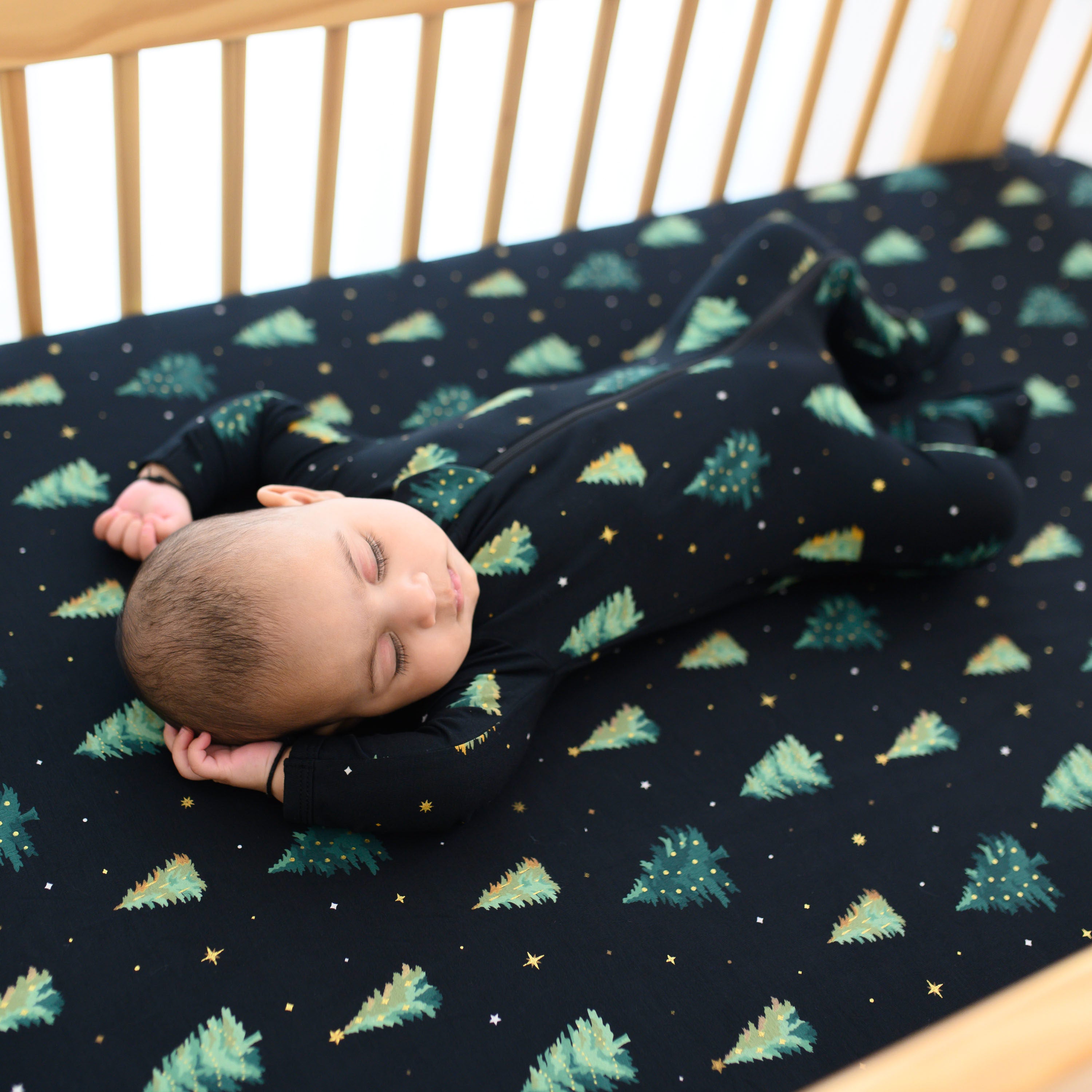 Sleeping infant laying in a crib on the Crib Sheet in Twinkle Tree wearing a matching zippered footie