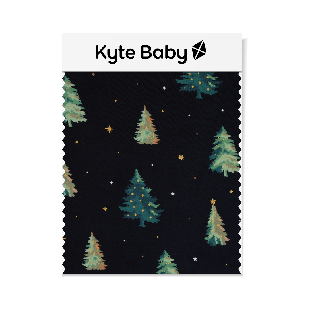 A swatch of Kyte Baby's Twinkle Tree print featuring two different colored trees and gold and white stars on a black background